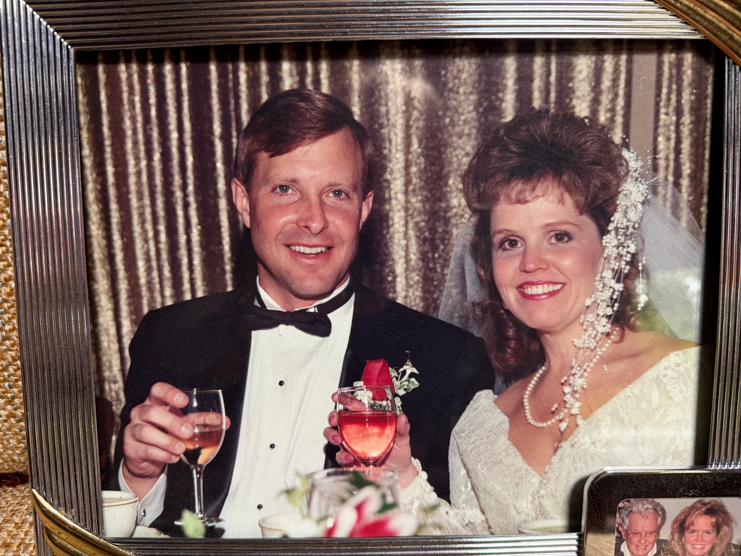 Smiling newlywed couple in tuxedo and wedding dress toasting with wine glasses at their reception.