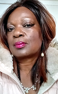 Close-up portrait of a woman with shoulder-length brown hair, pink lipstick, and a pearl necklace wearing a light fur-lined coat.