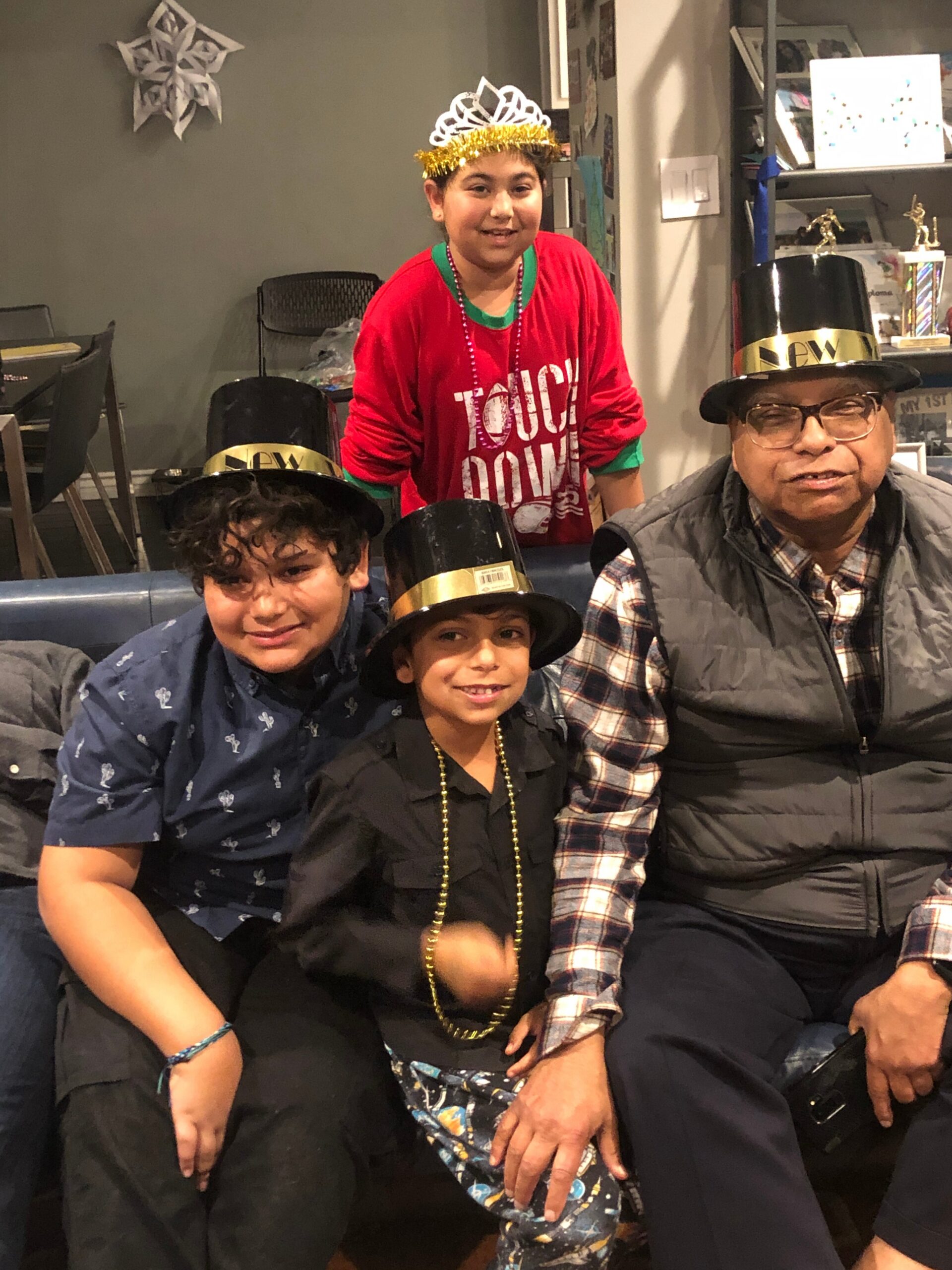 Group of friends and family posing indoors in festive attire with party hats, a tiara, and bead necklaces.