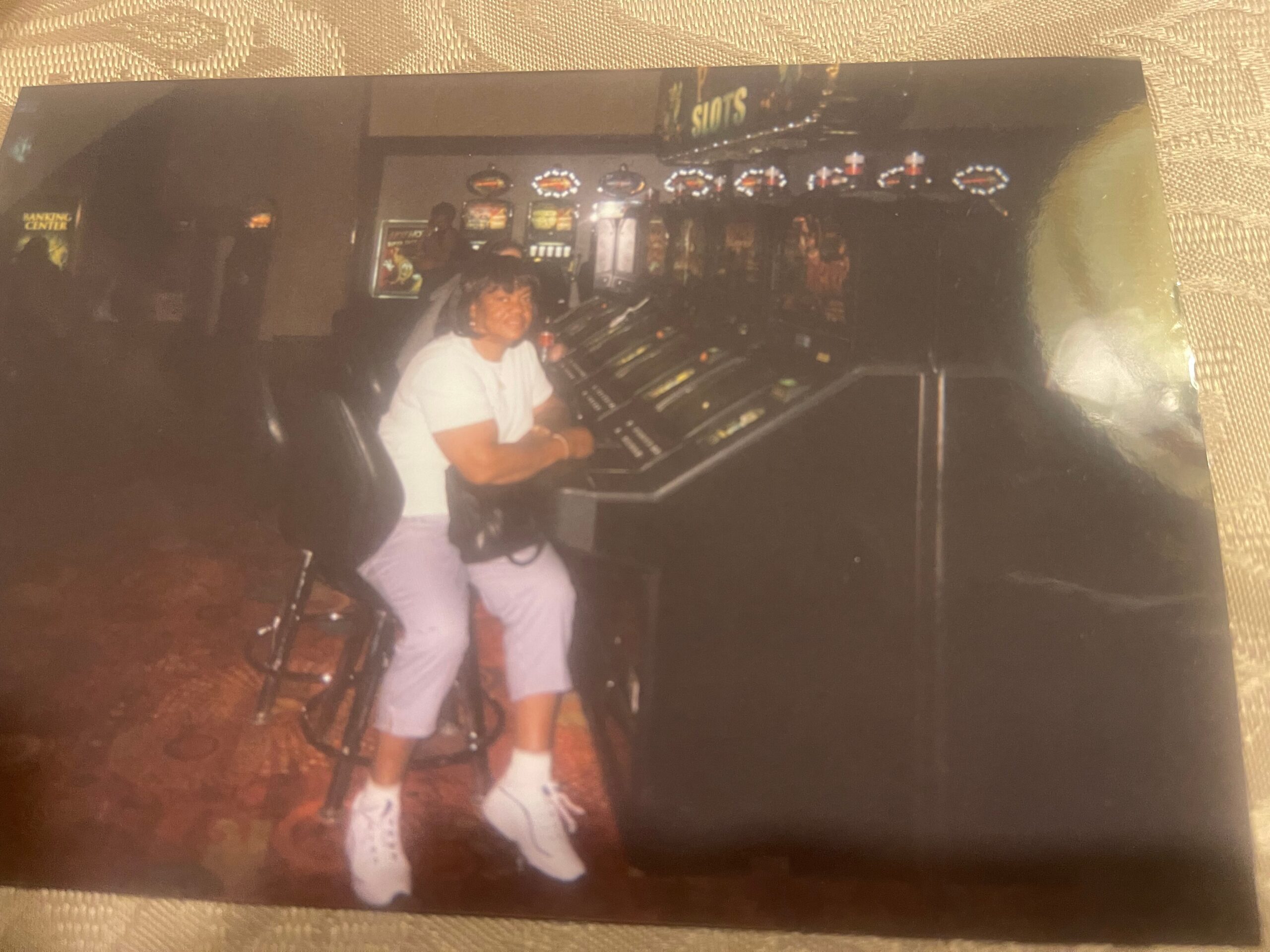 Person in a white shirt and light shorts standing at a row of slot machines in a casino, smiling at the camera.