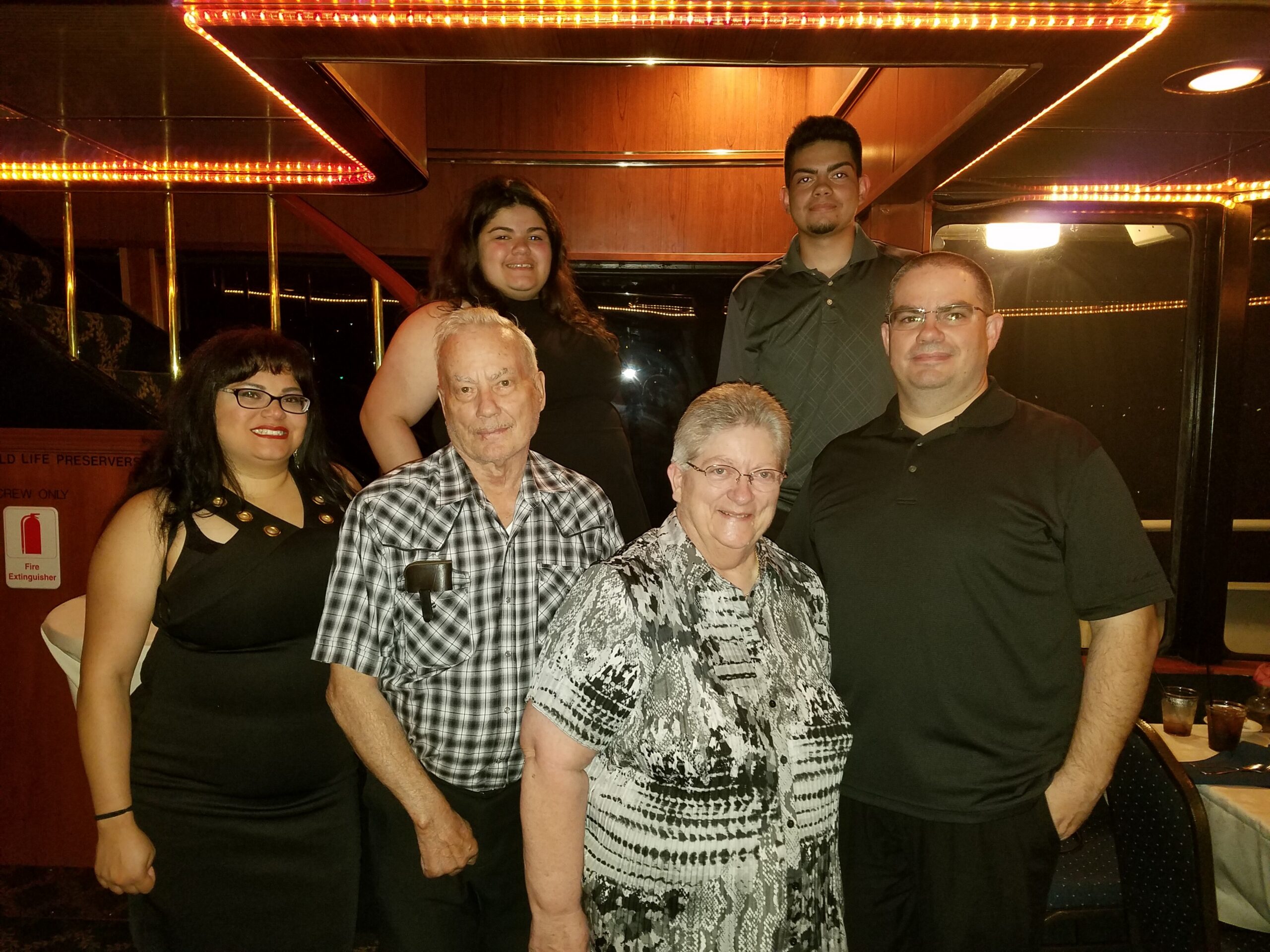 Six adults posing together inside a party bus with warm orange LED lighting overhead.