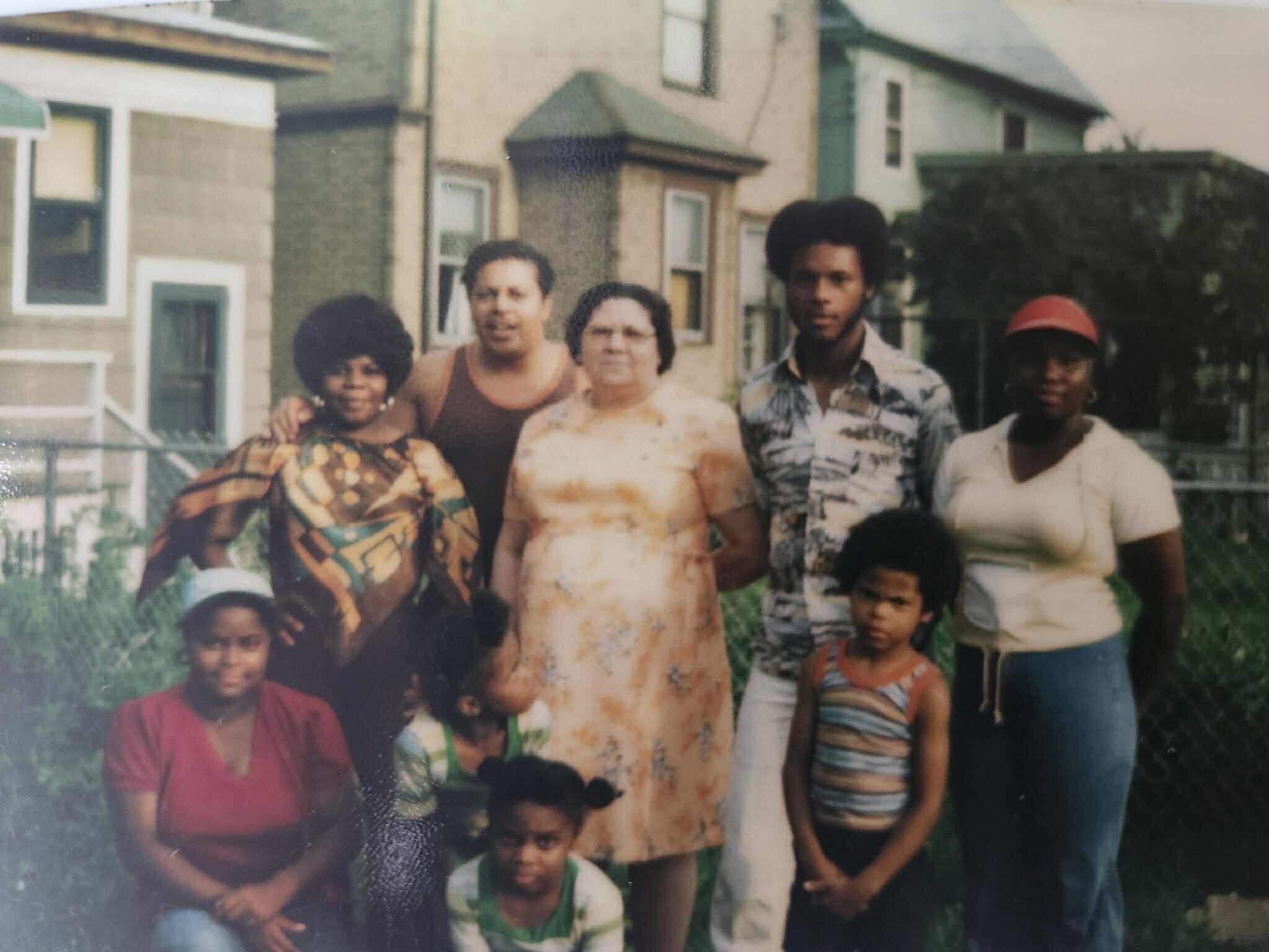 A group of adults and children posing together outdoors in front of townhouses, smiling for the camera.