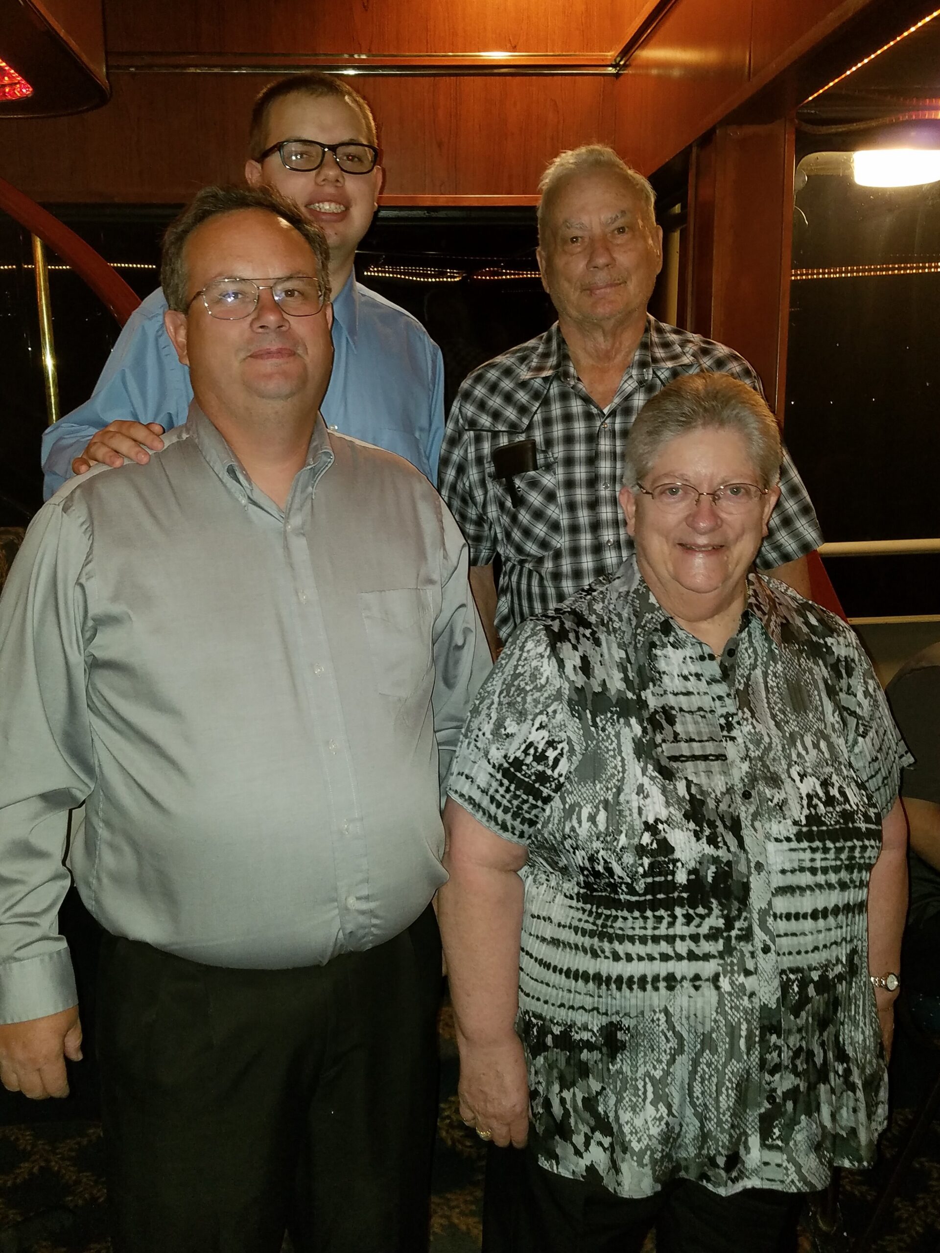 Group of four adults posing together inside a wood-paneled boat cabin, smiling for the photo at night.