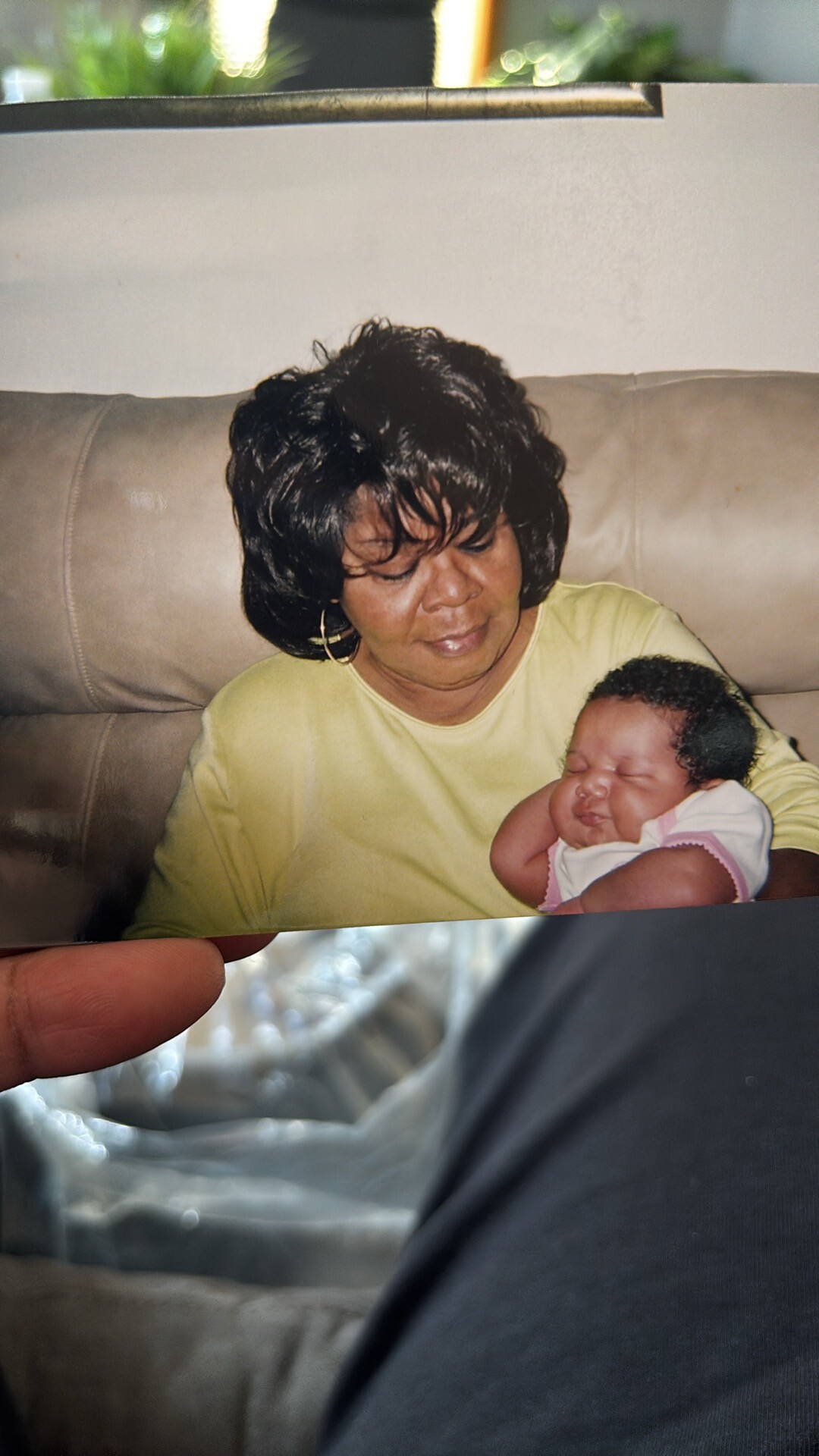 Woman with short black hair cradling a sleeping newborn on a beige couch.