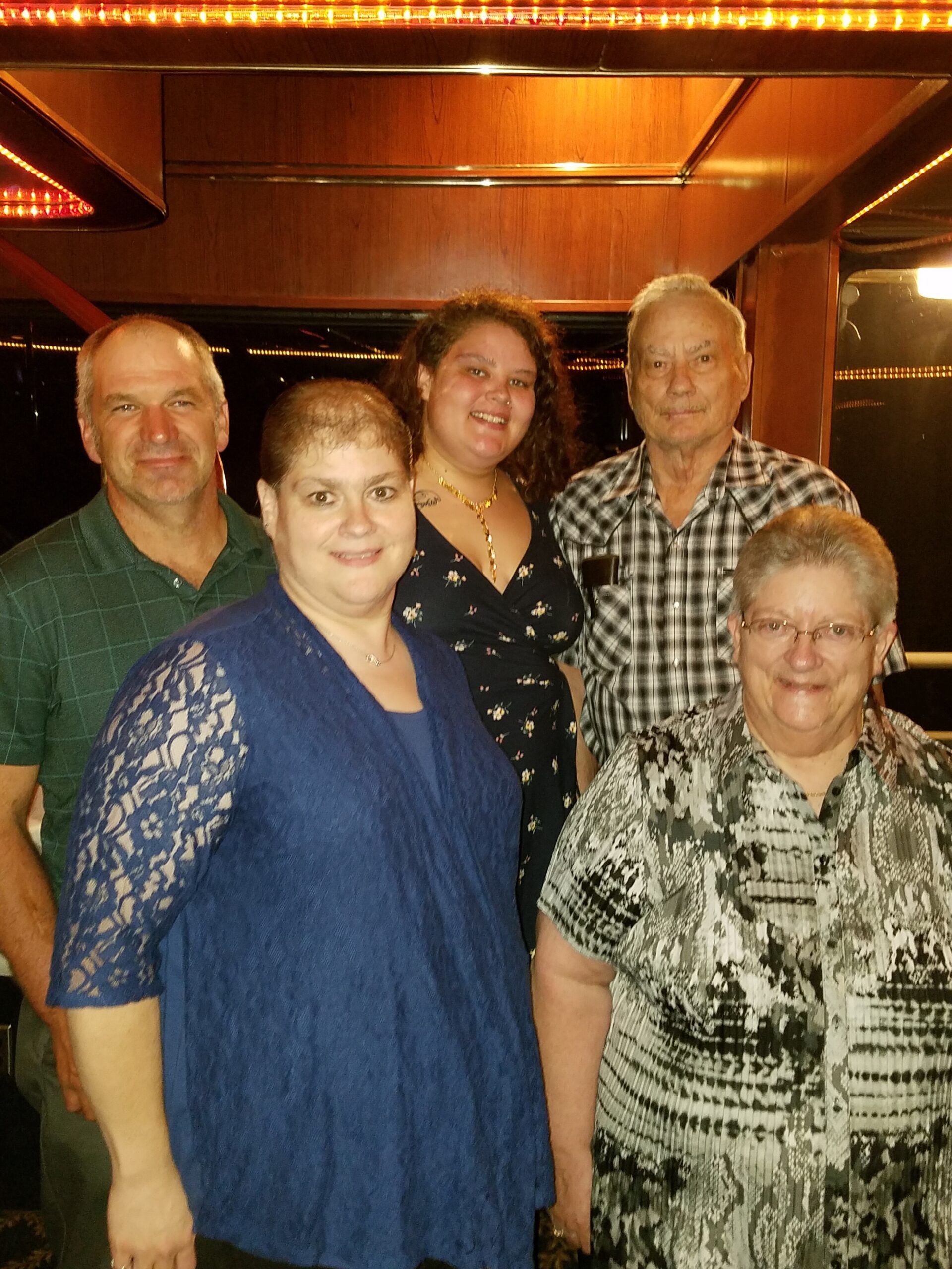 Five adults pose together indoors, smiling, in a warm wood-paneled room with orange lighting behind them.
