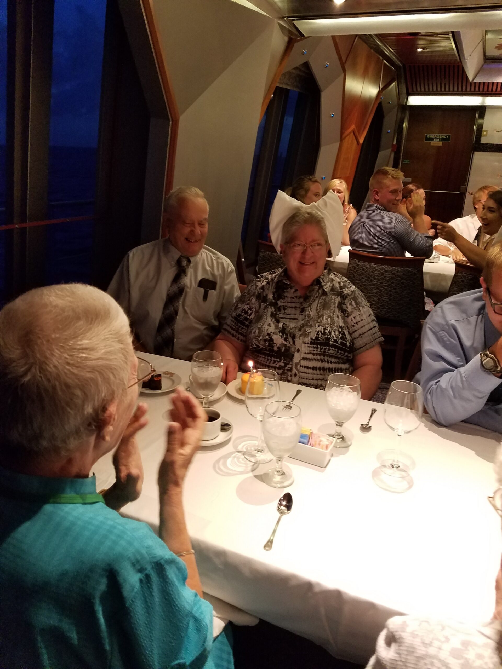 Guests seated at a candlelit dining table on a cruise ship, smiling and chatting during a group meal.
