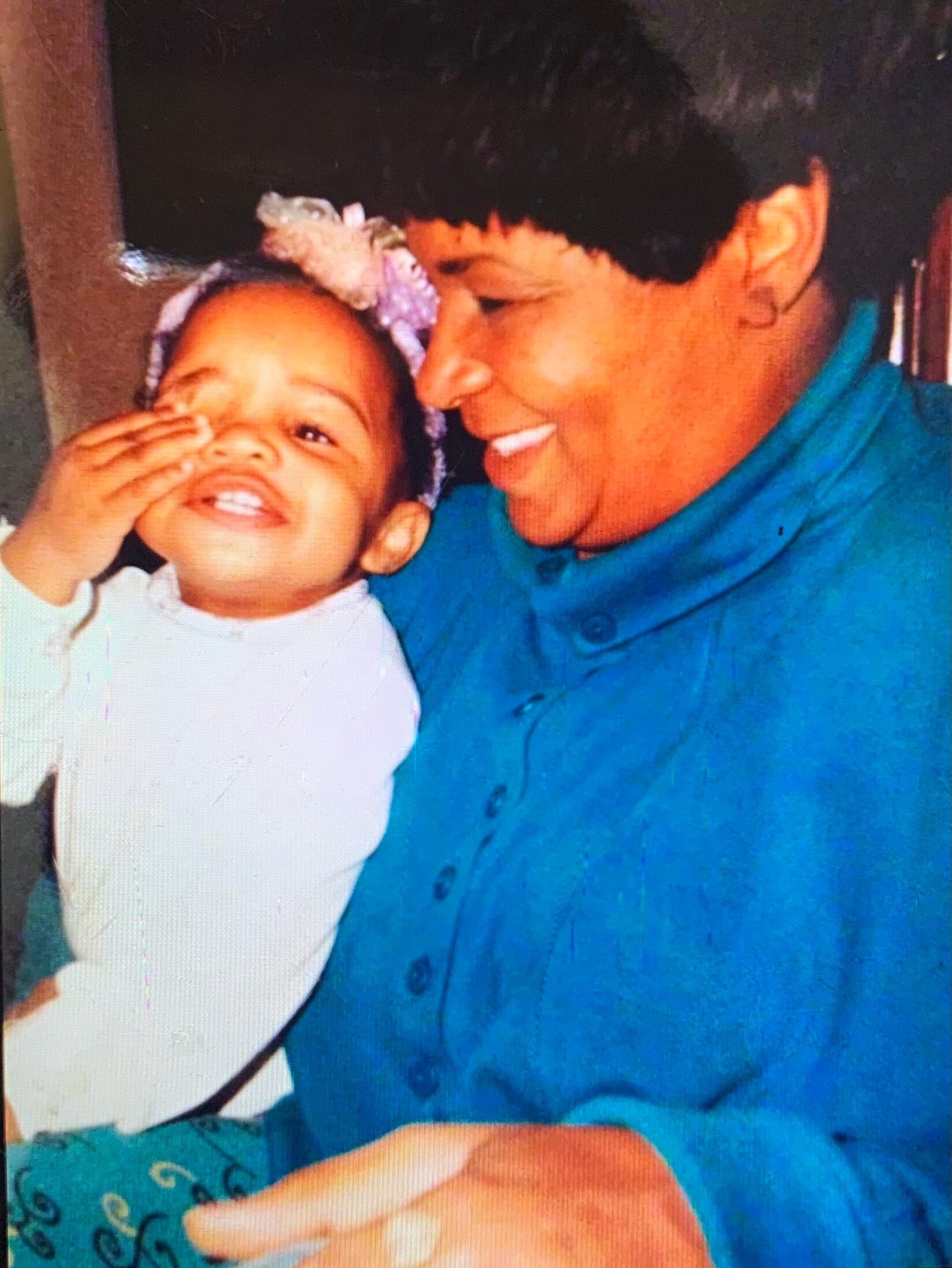 A man in a teal shirt smiles as he holds a baby wearing a purple floral headband.