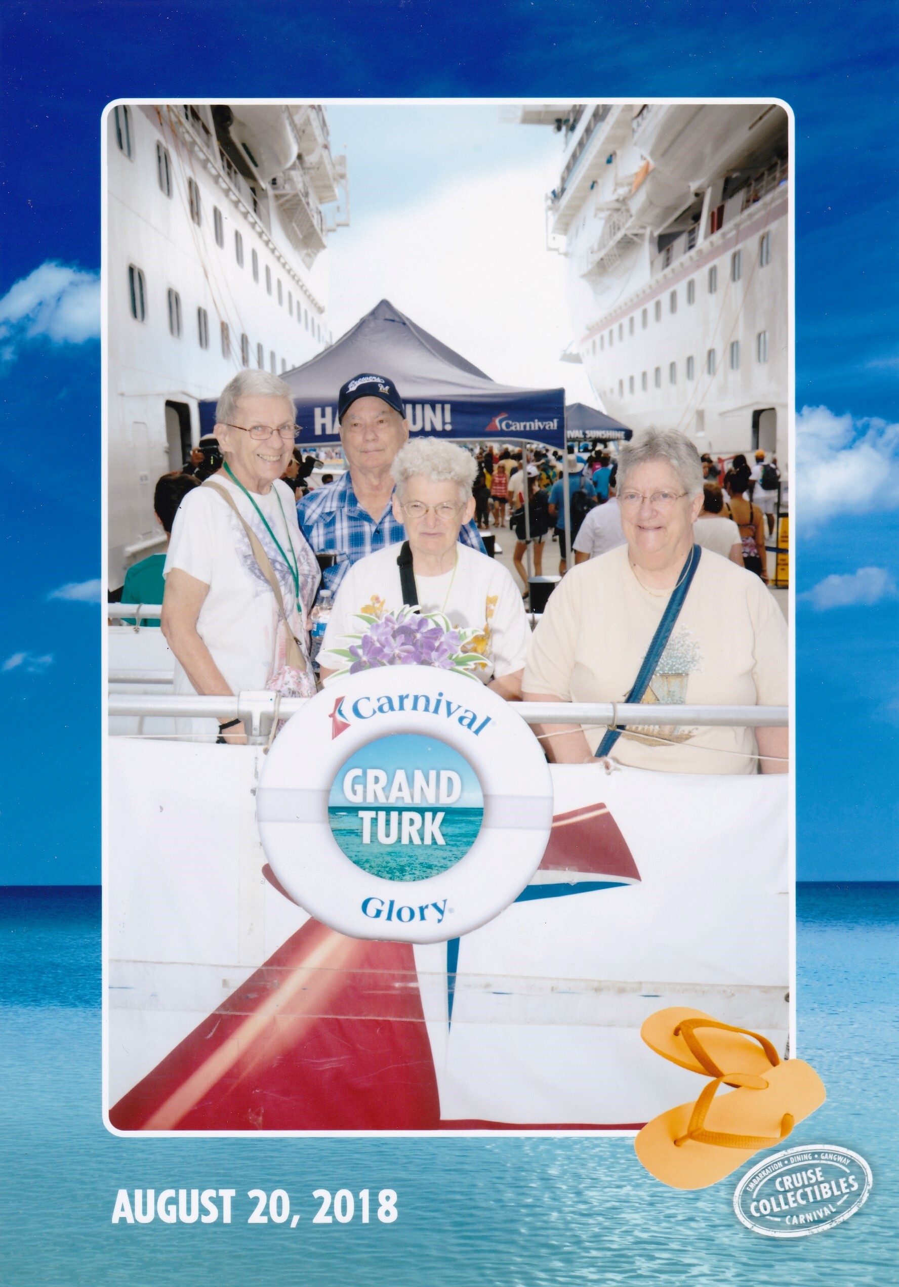 Four seniors posing and smiling at a Carnival cruise ship photo booth with a Grand Turk sign, August 20, 2018, blue ocean backdrop.