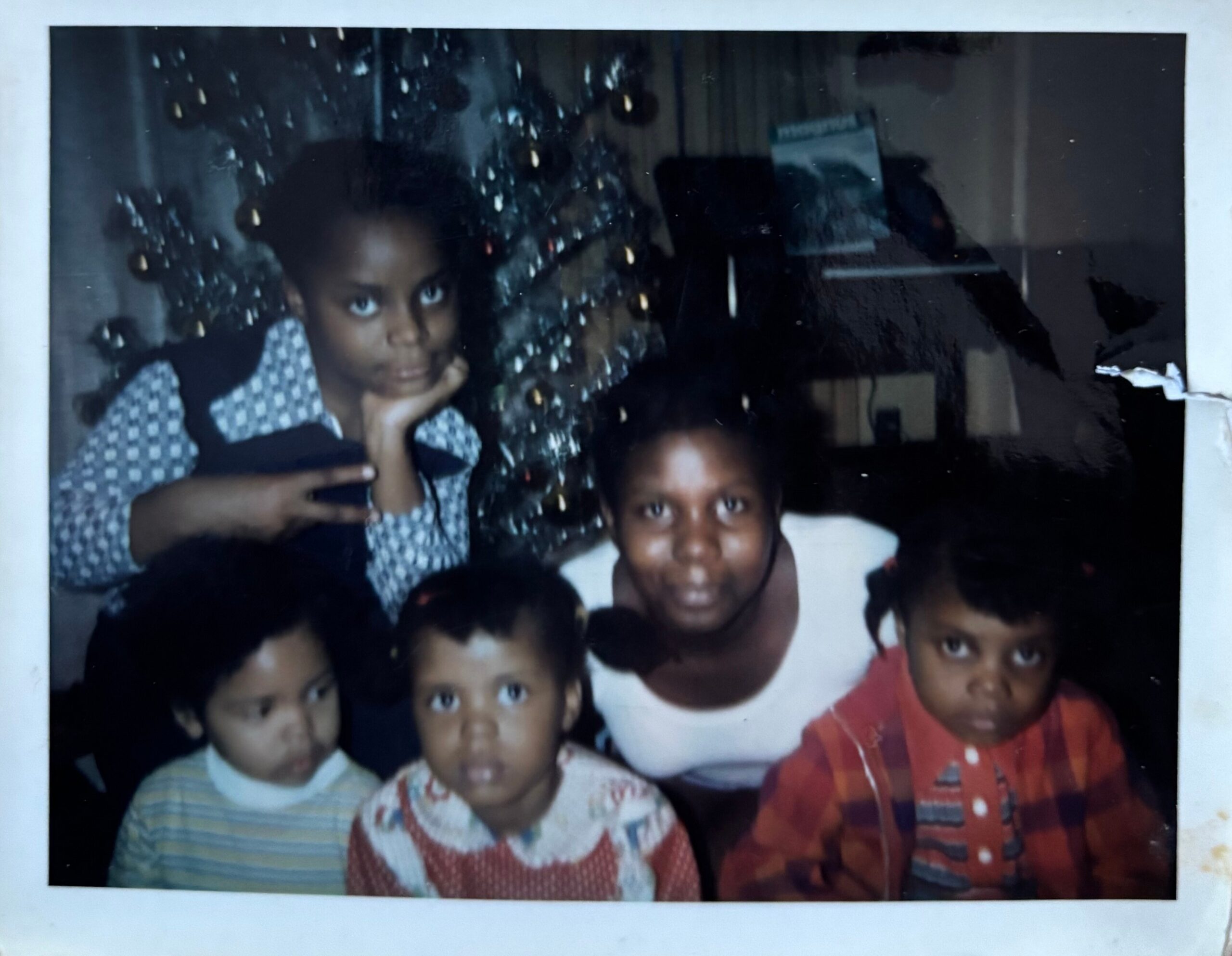 Group of children posing closely for a photo indoors, some wearing patterned shirts and looking at the camera.