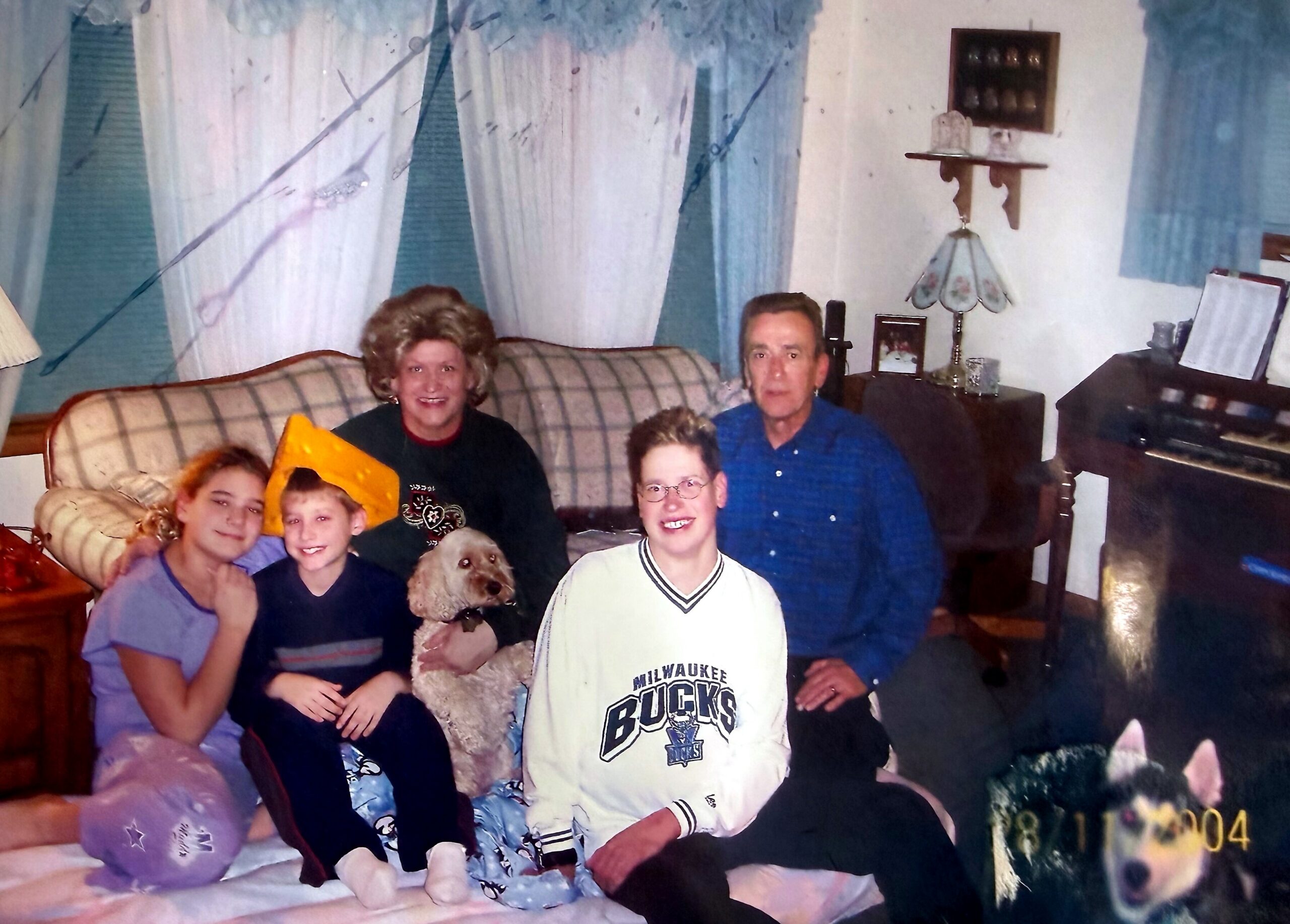 Family group posing on a plaid couch in a living room with a dog in front, holiday decor visible in the background.
