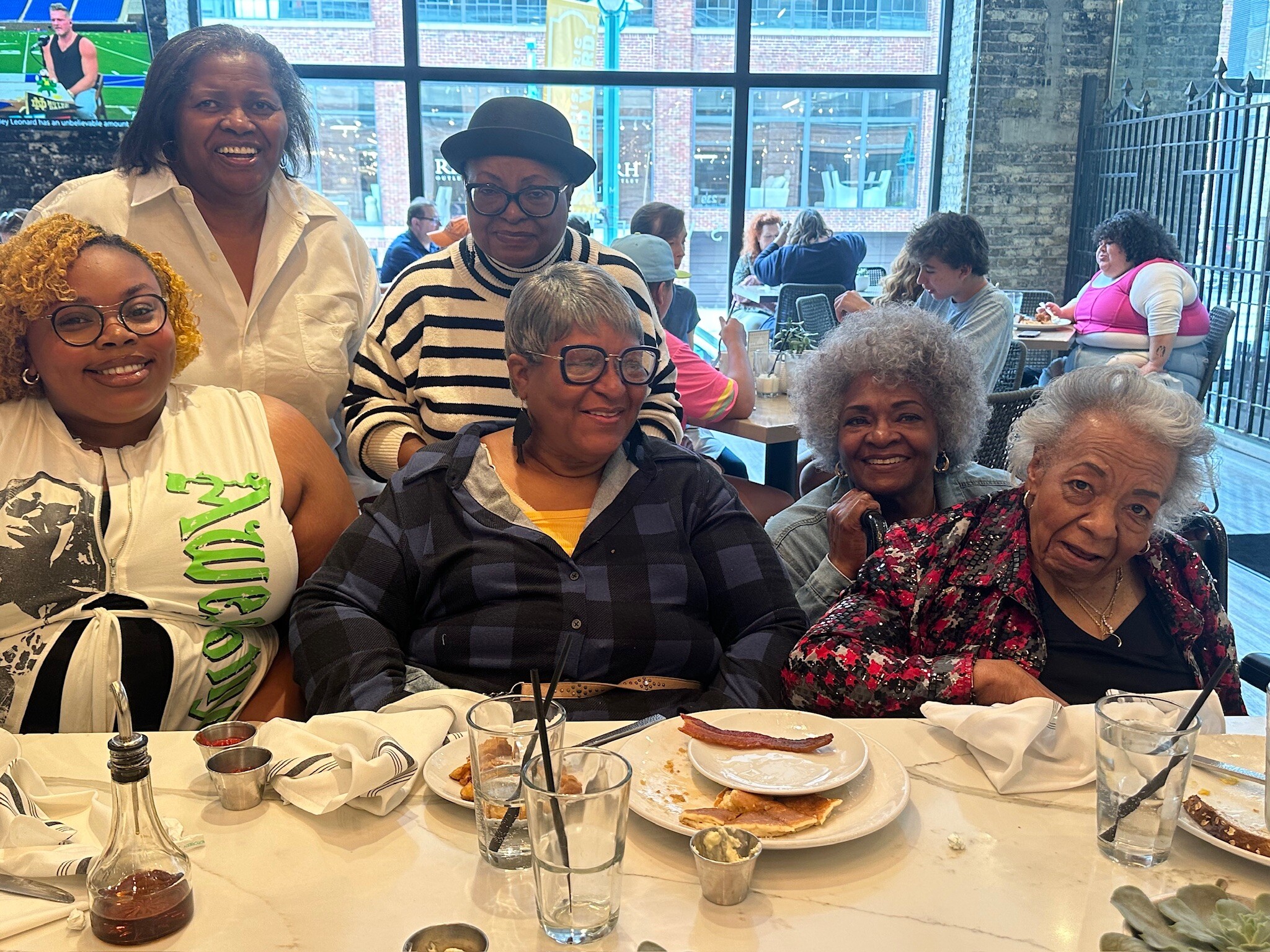 Group of smiling adults seated around a restaurant table with plates, glasses, and condiments, posing for a photo.