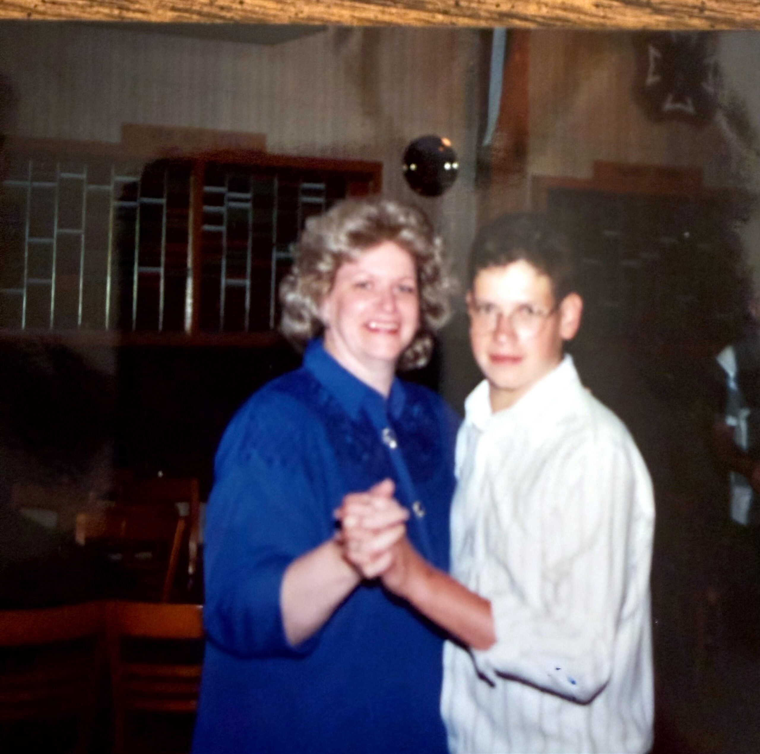 Two smiling people stand side by side, their hands clasped together in front in a friendly pose.