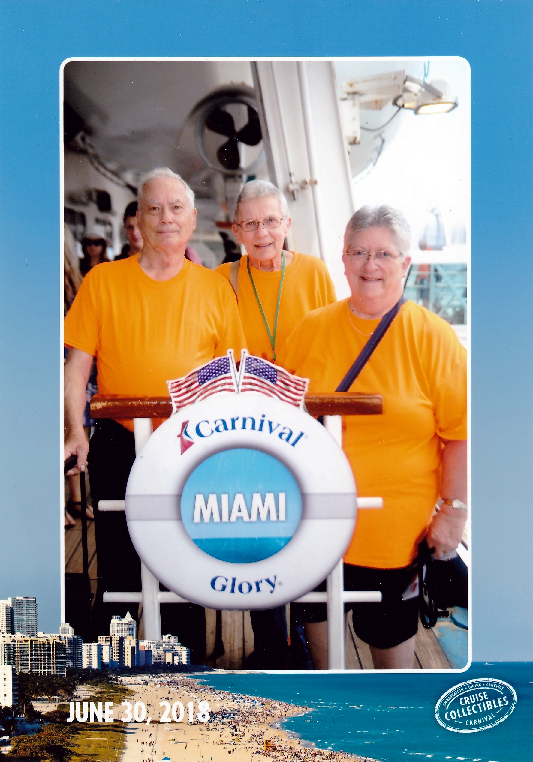 Three people in orange shirts pose on a cruise ship deck with a Miami sign and a Carnival life ring in front of them.