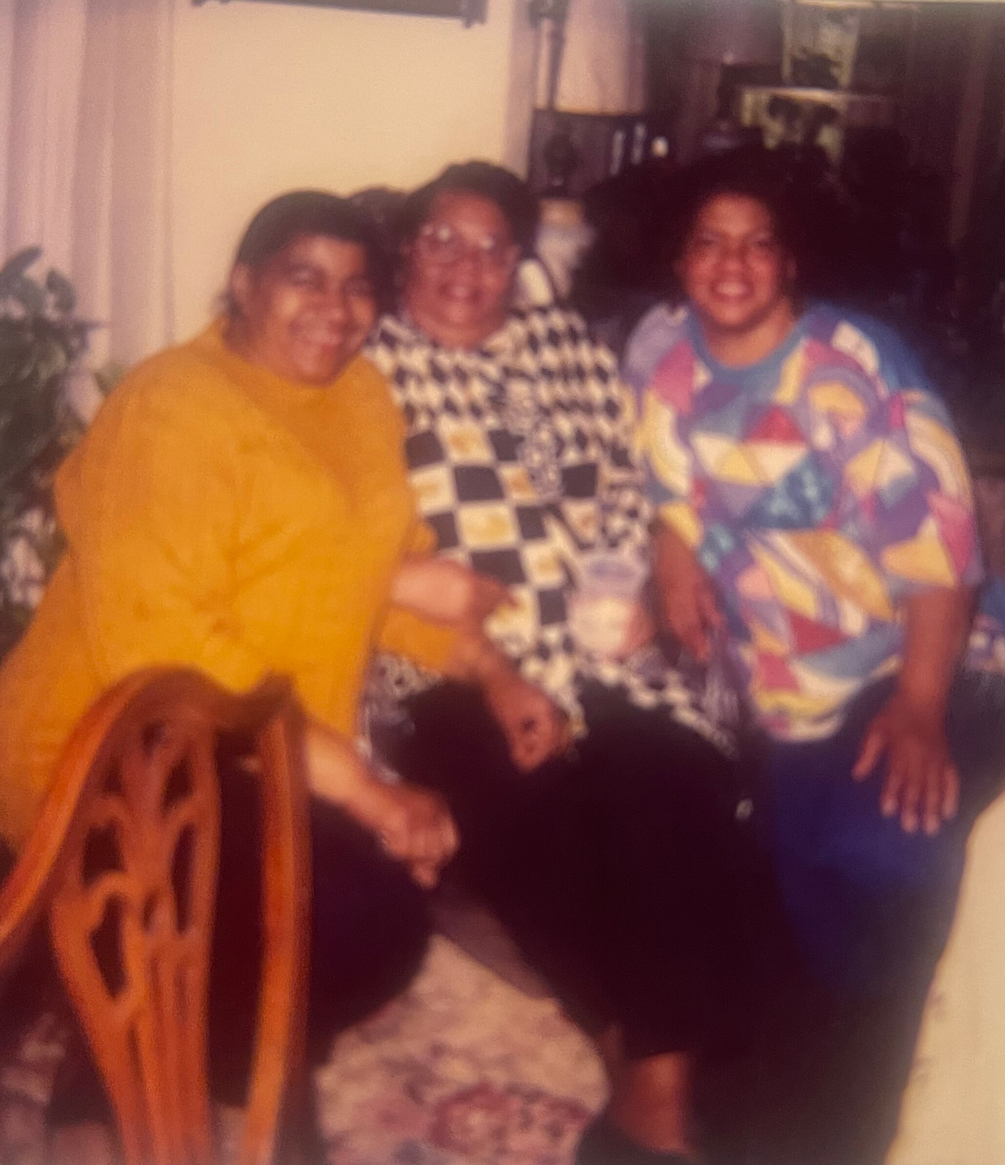 Three people posing together indoors, smiling for a casual group photo, wearing colorful outfits.