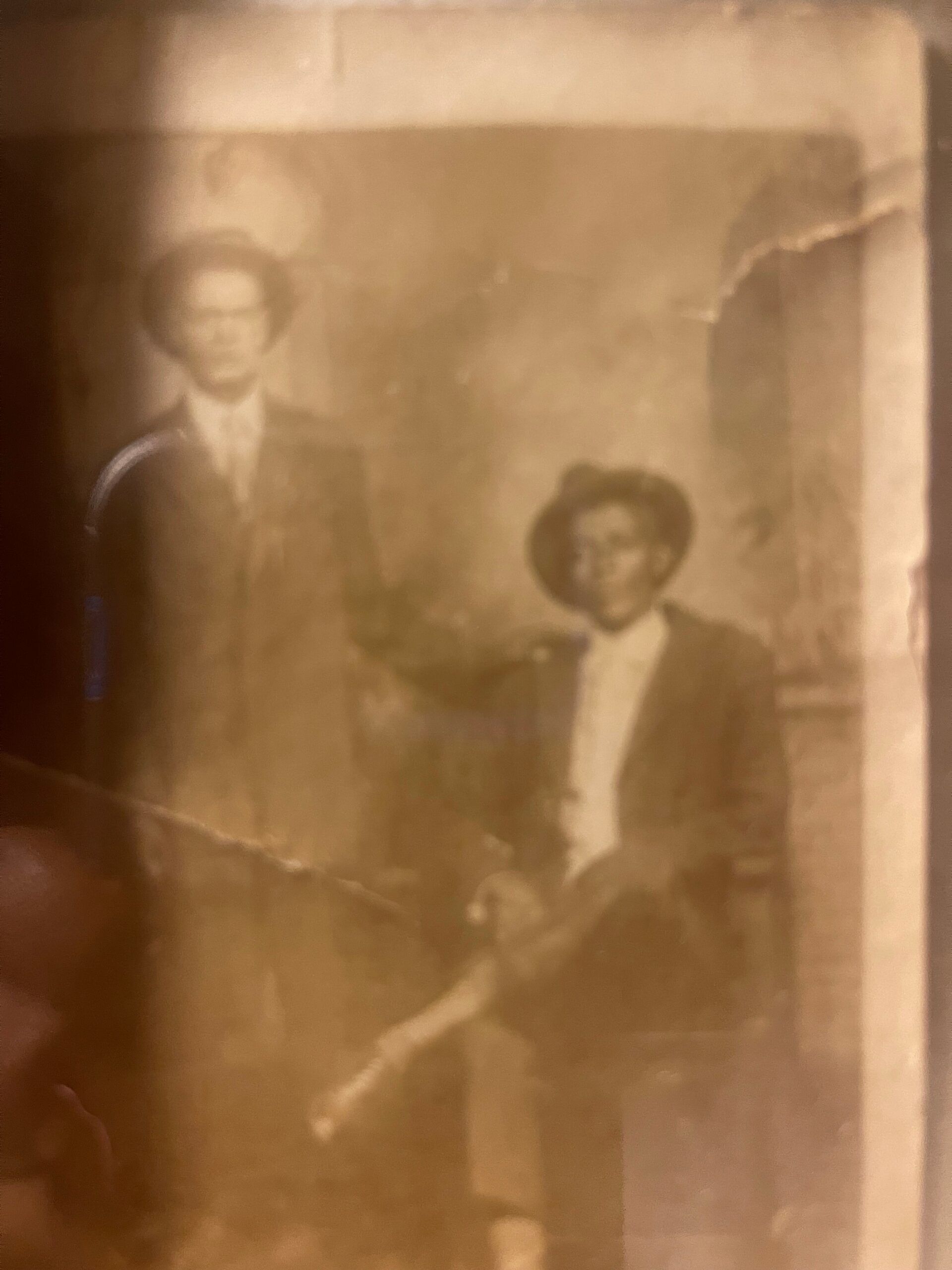 Blurry sepia-toned portrait of a man with glasses and a younger person beside him in formal attire, inside a frame.
