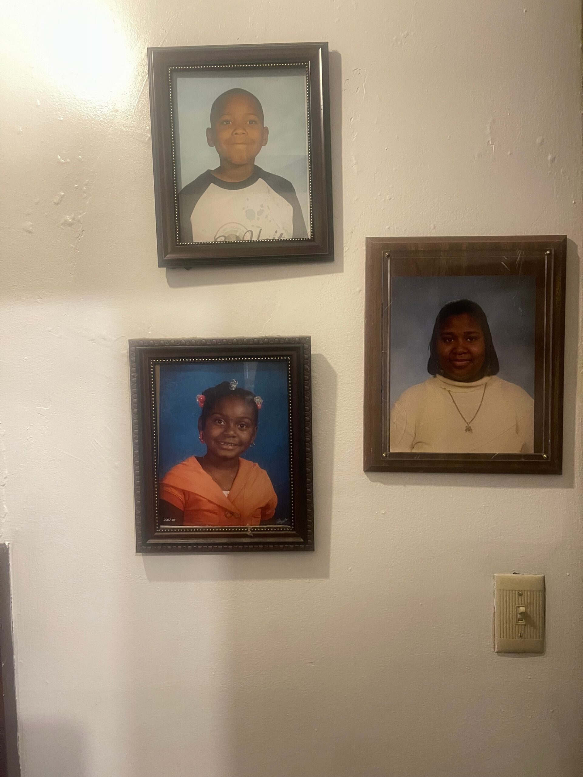 Wall display of four framed portraits of children hanging on a light wall, two on the left and two on the right, showing smiling young faces in formal poses.