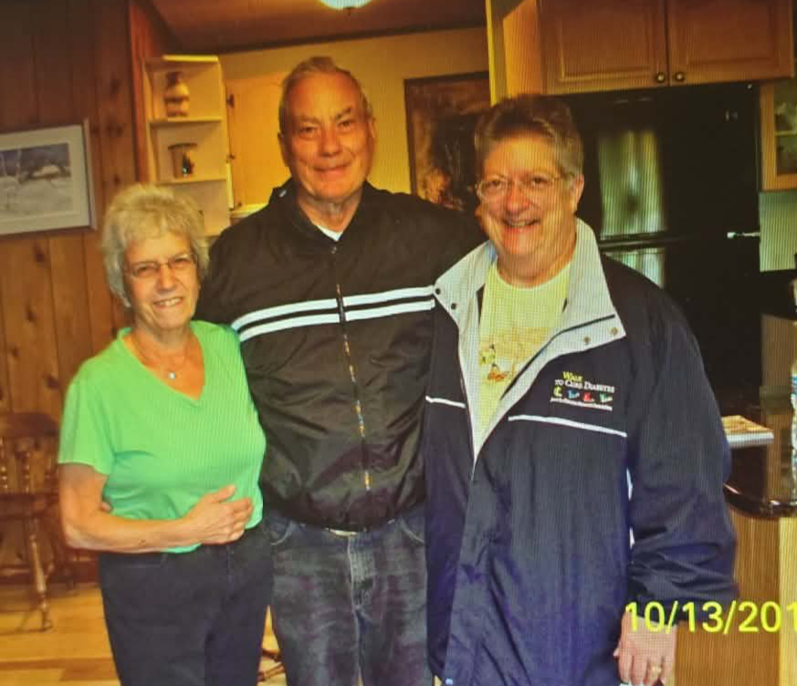 Three smiling seniors pose together in a cozy home kitchen, standing shoulder to shoulder.