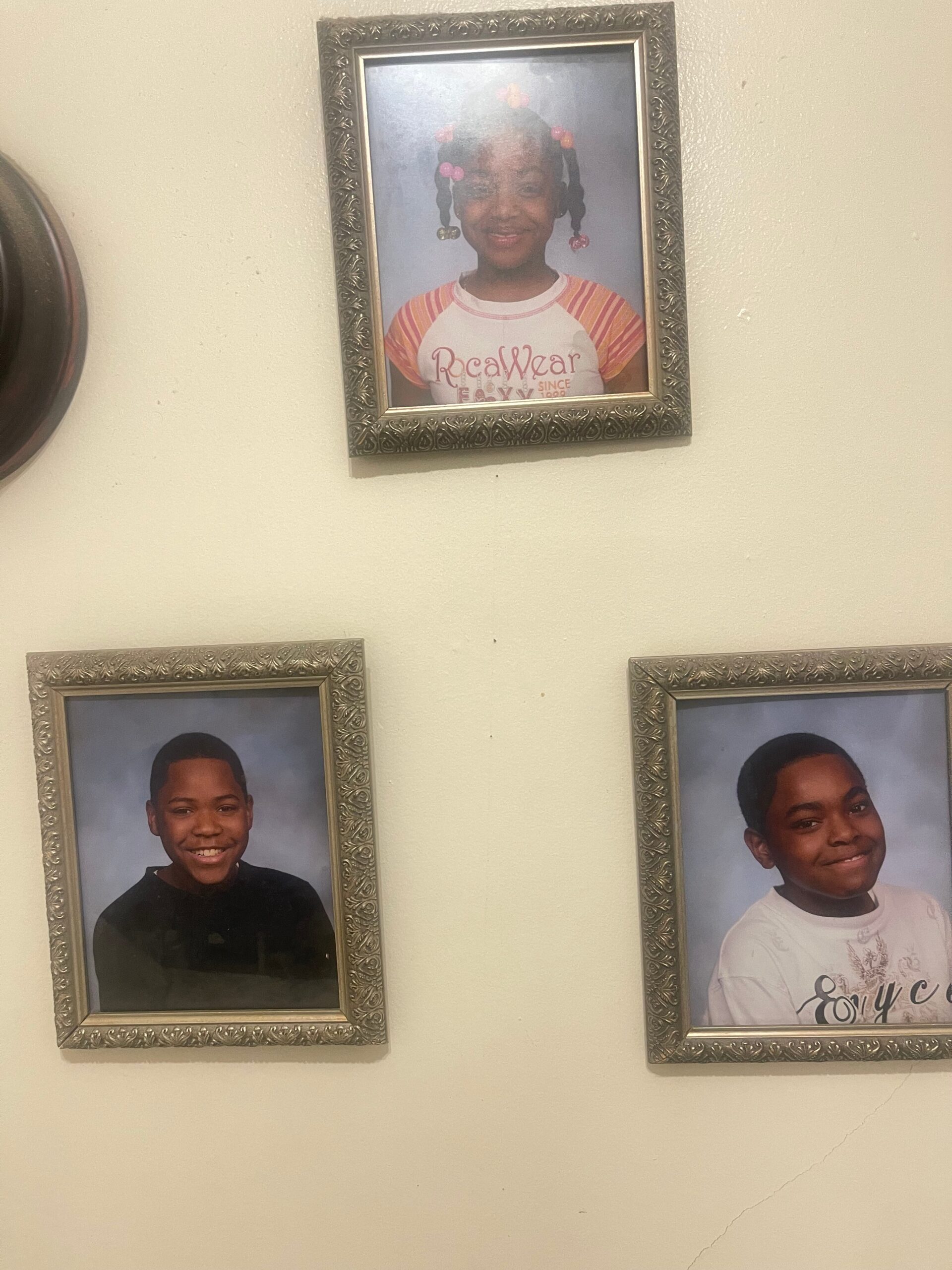 Framed school portrait of a smiling girl with colorful pigtails on a beige wall, surrounded by other framed photos on the wall.