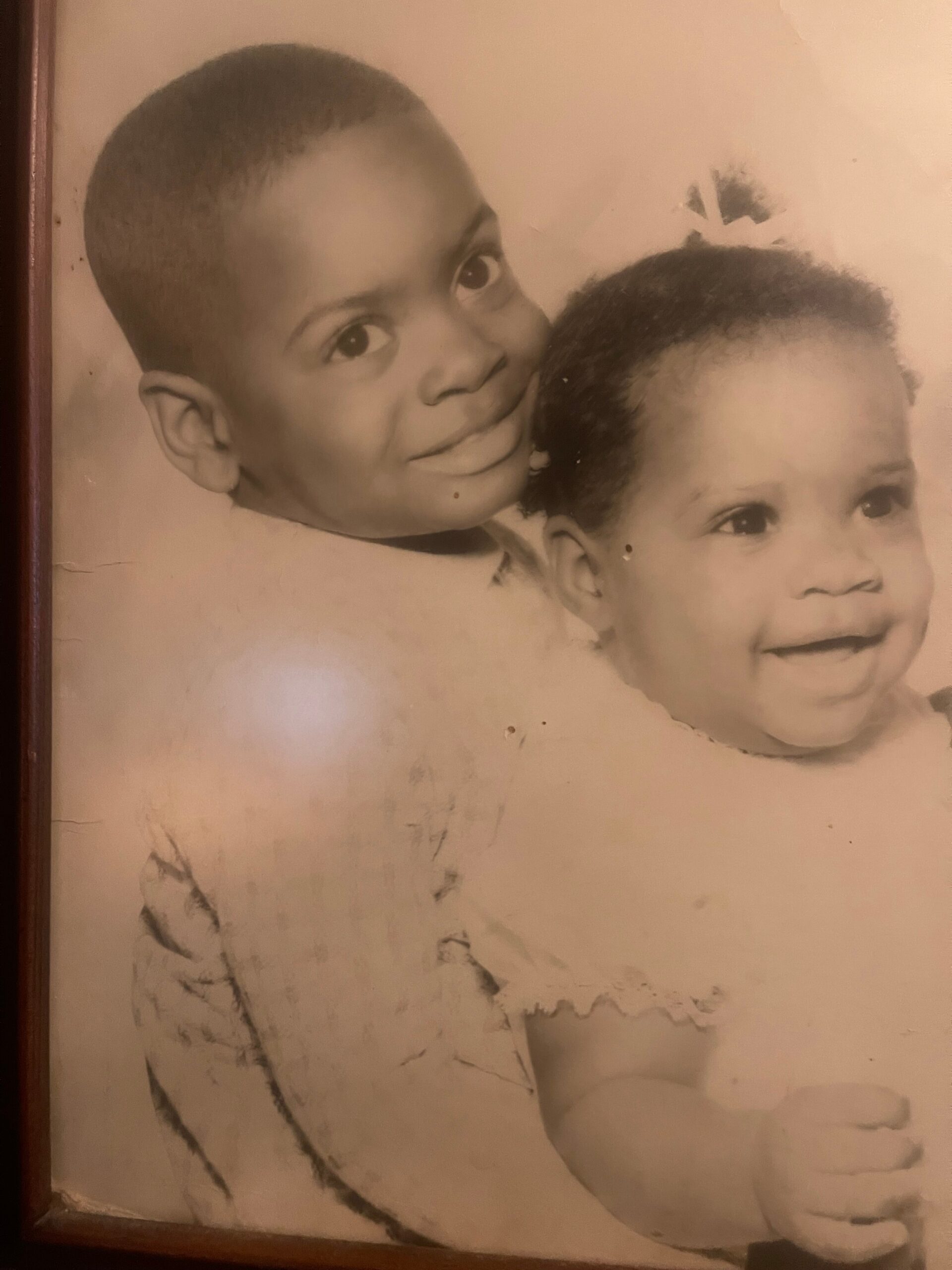 Two smiling children in a sepia-toned portrait: a boy on the left and a girl with a short fro on the right.