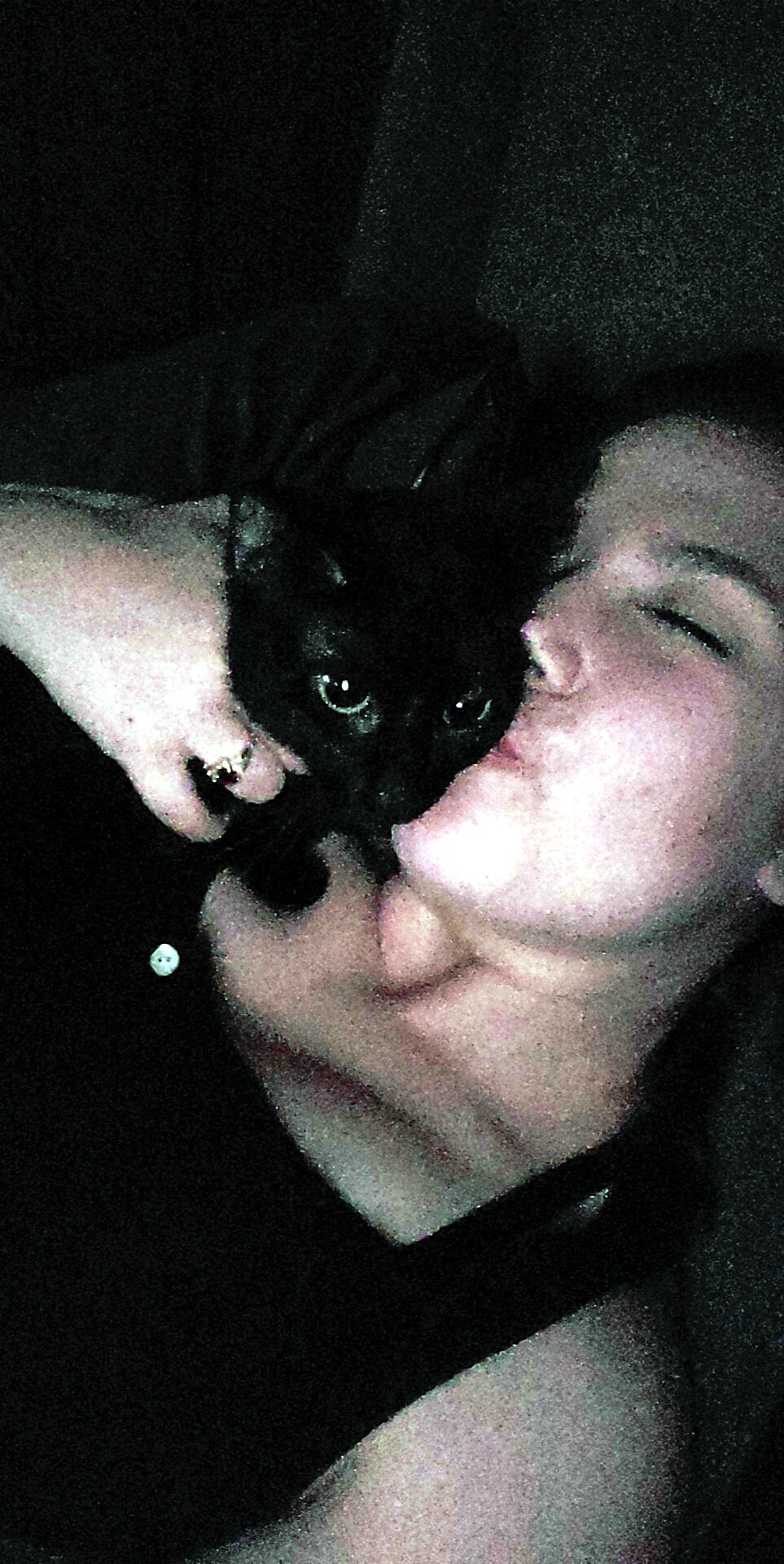 Close-up of a person kissing a black cat on the cheek in dim lighting.