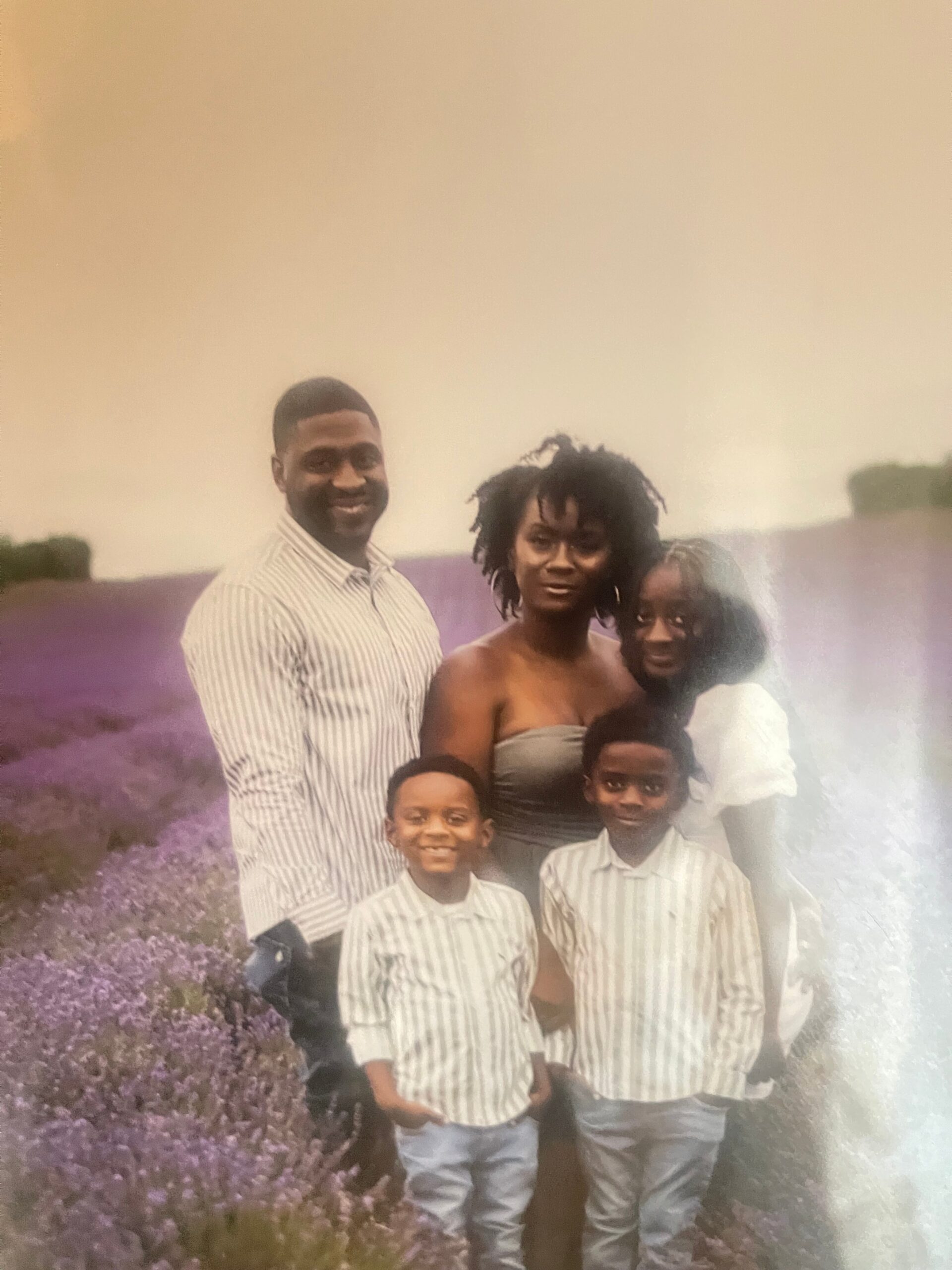 A smiling family of six posing together in a lavender field, with tall purple flowers in the foreground.