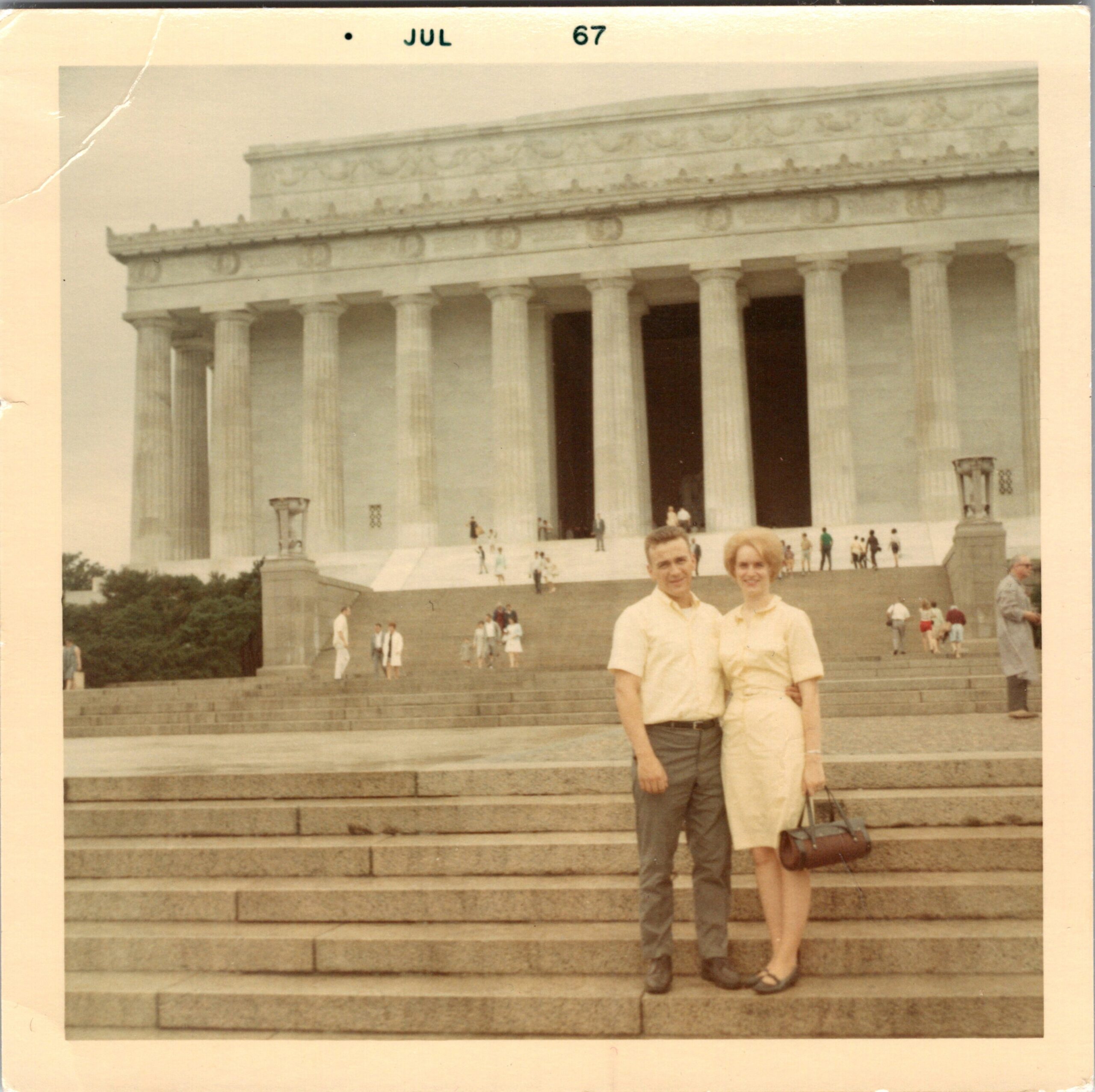 Couple posing on the steps of a large neoclassical temple with tall columns; tourists in the background, July 1967.