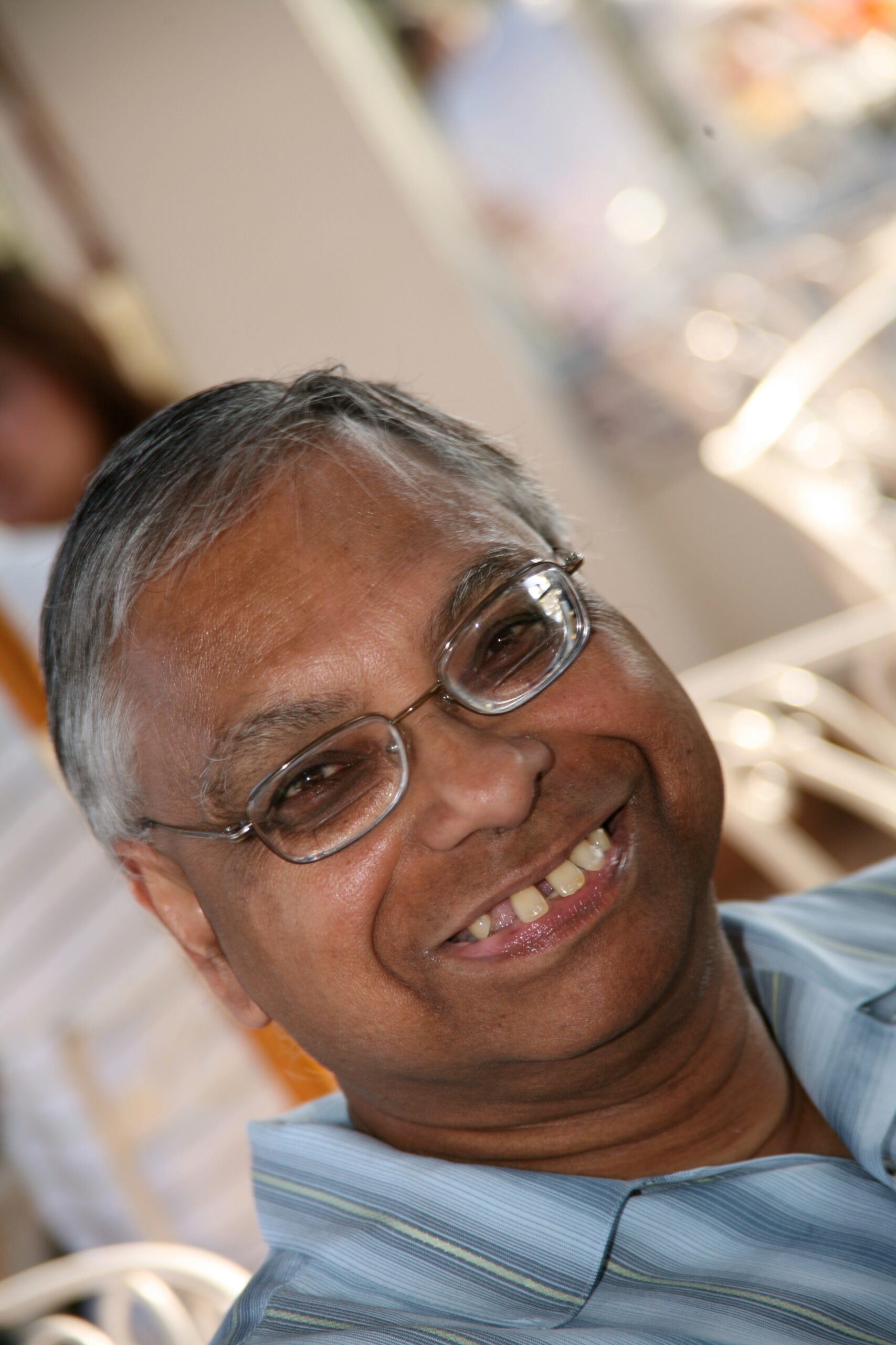 Smiling man with short gray hair and glasses, wearing a blue striped shirt, tilted head toward the camera.
