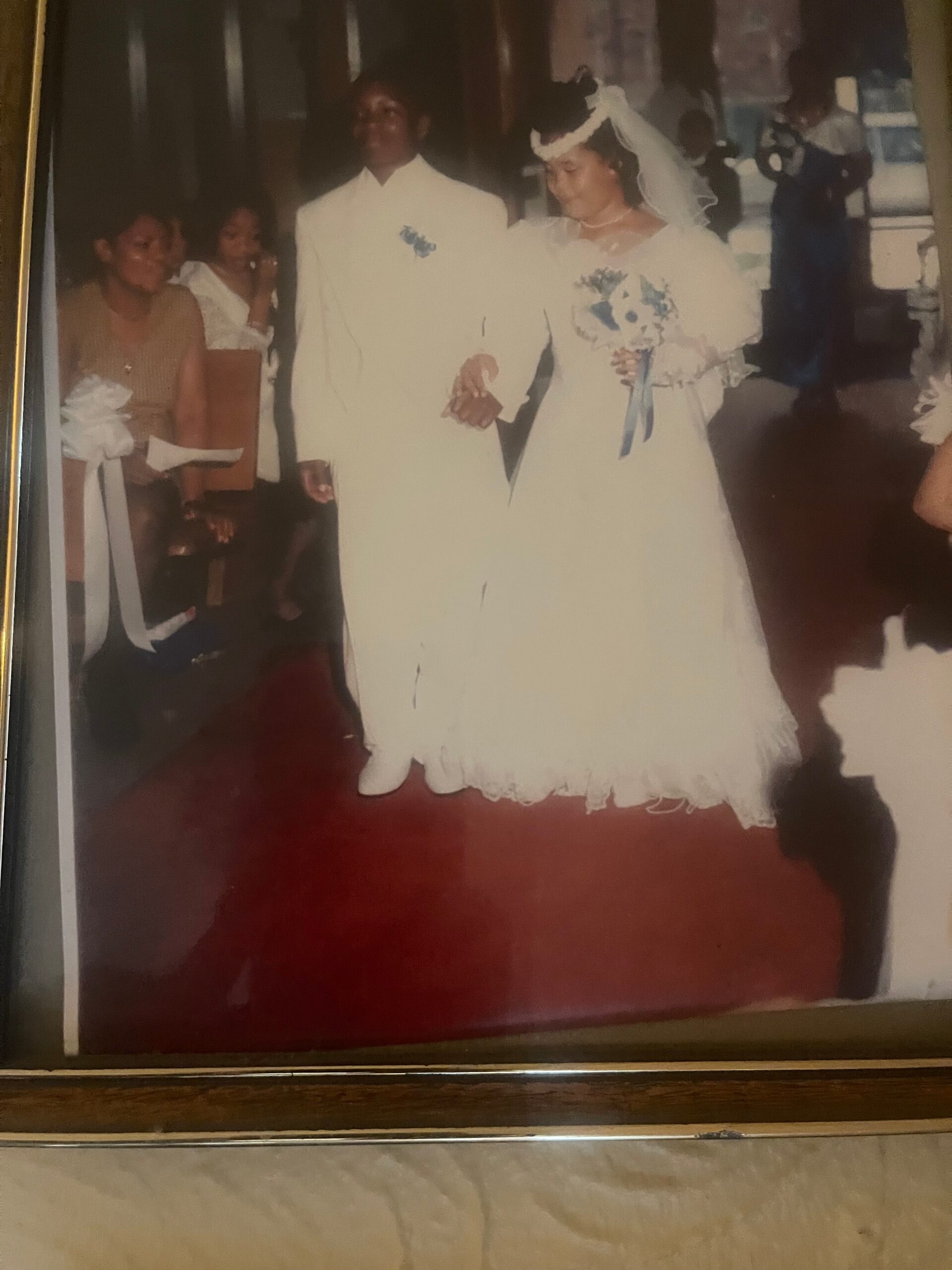 Bride and groom in wedding attire walking arm in arm, guests in the background at a ceremony.