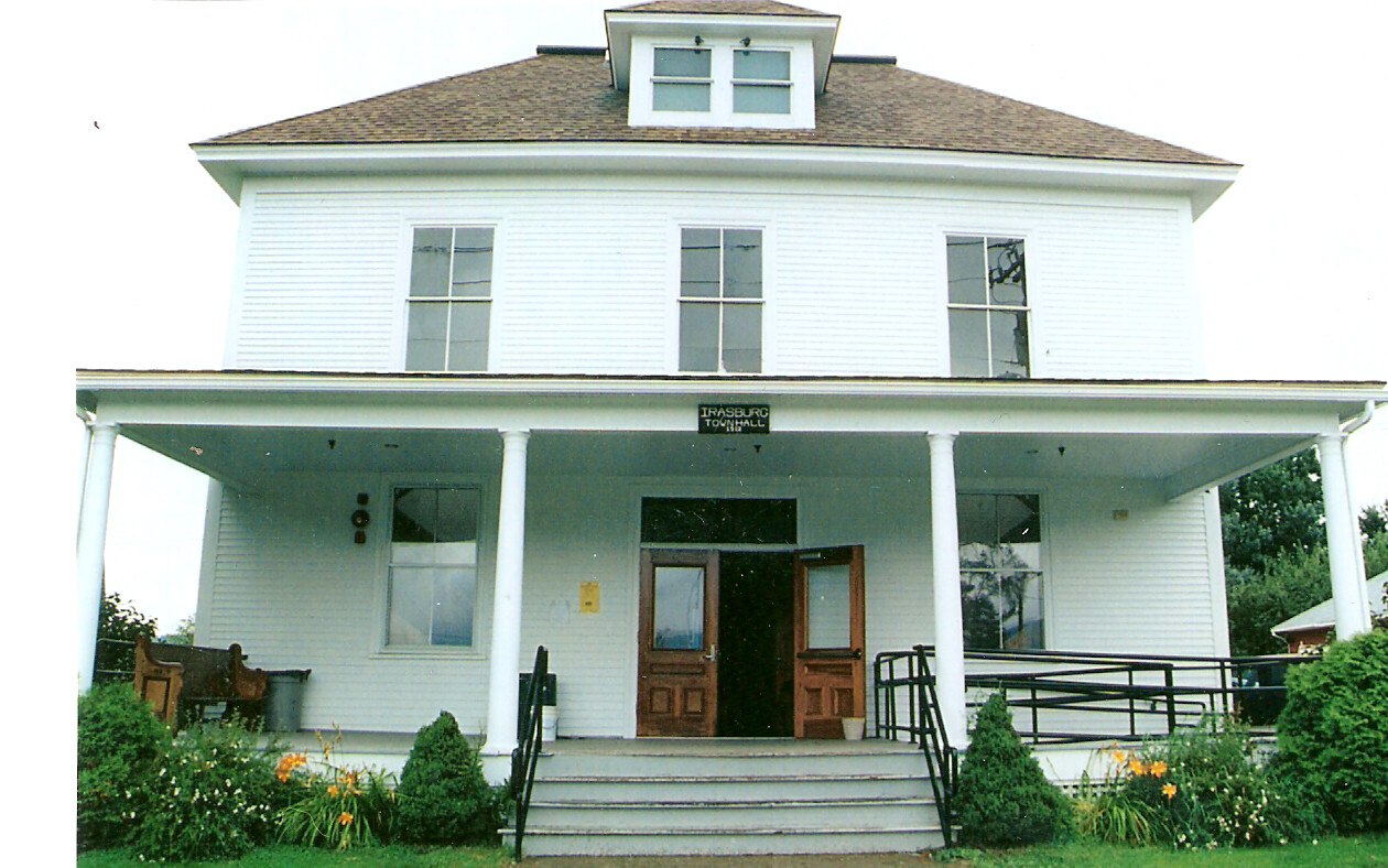 White two-story town hall with a covered front porch, six steps to double wooden doors, and a wheelchair ramp on the right.