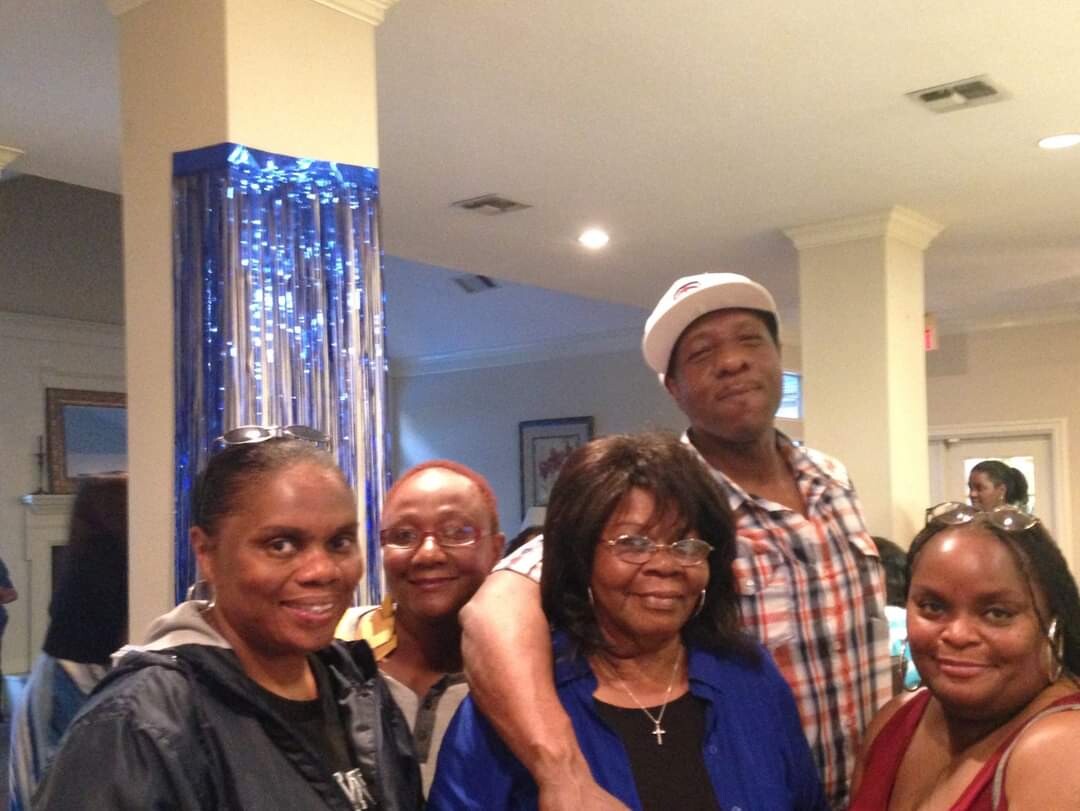 Group of five adults posing for a photo indoors, smiling at the camera with blue decorations in the background.