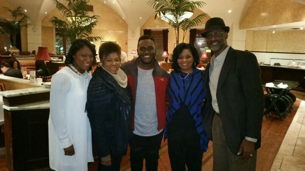 Five friends pose together in a warmly lit hotel restaurant lobby, smiling at the camera.