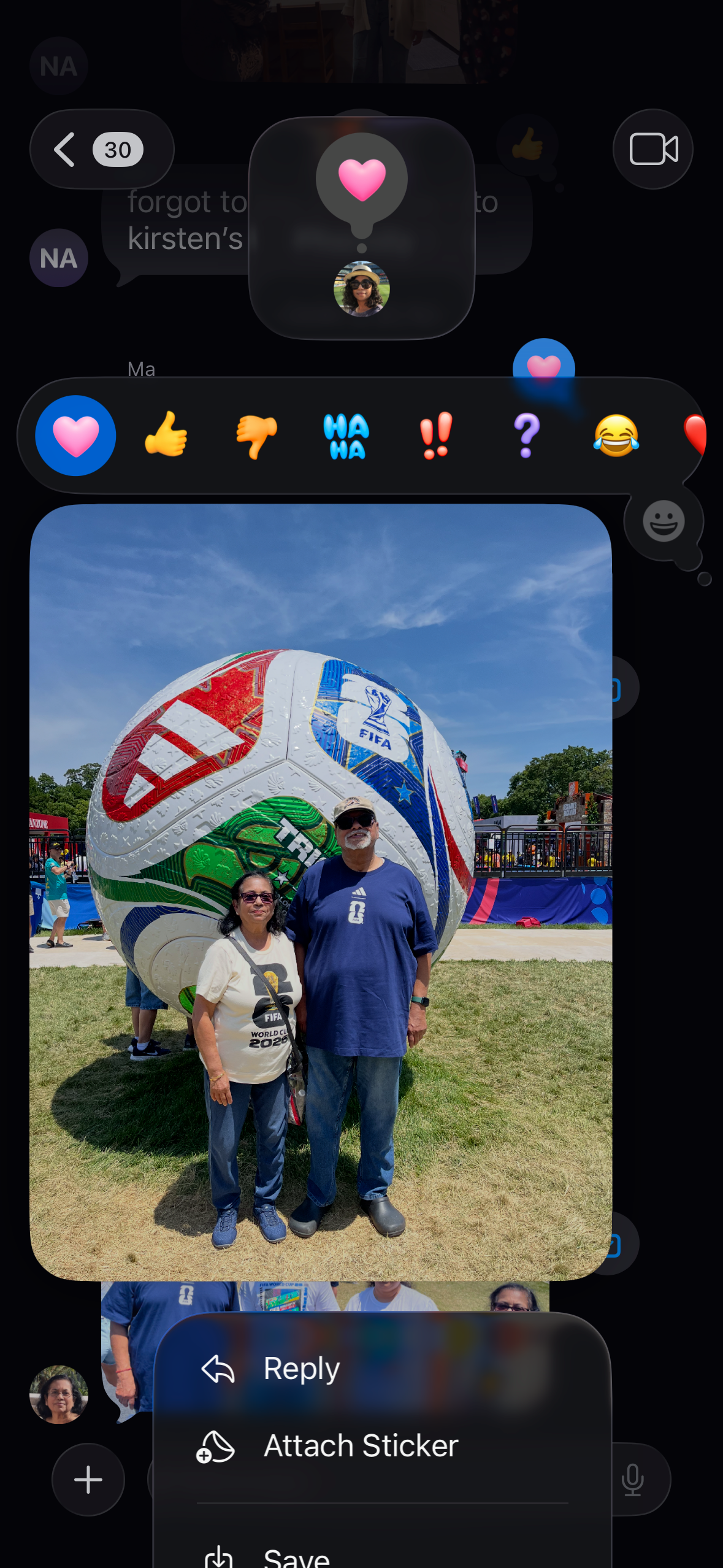 Two adults posing in front of a huge, colorful FIFA soccer ball at an outdoor event on a sunny day.