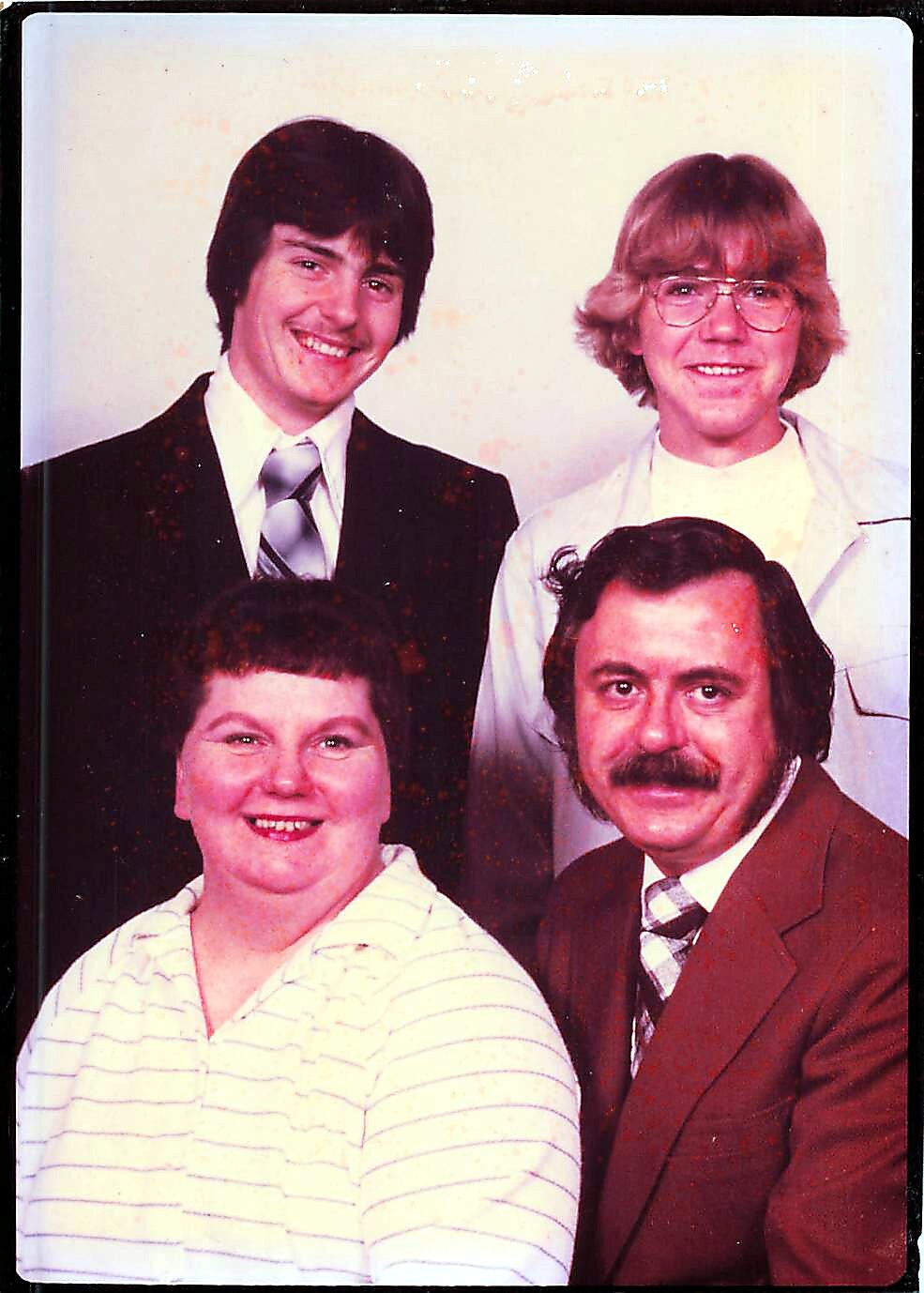 Group portrait of four adults posing together, two seated in front and two standing behind, all smiling in a studio setting.