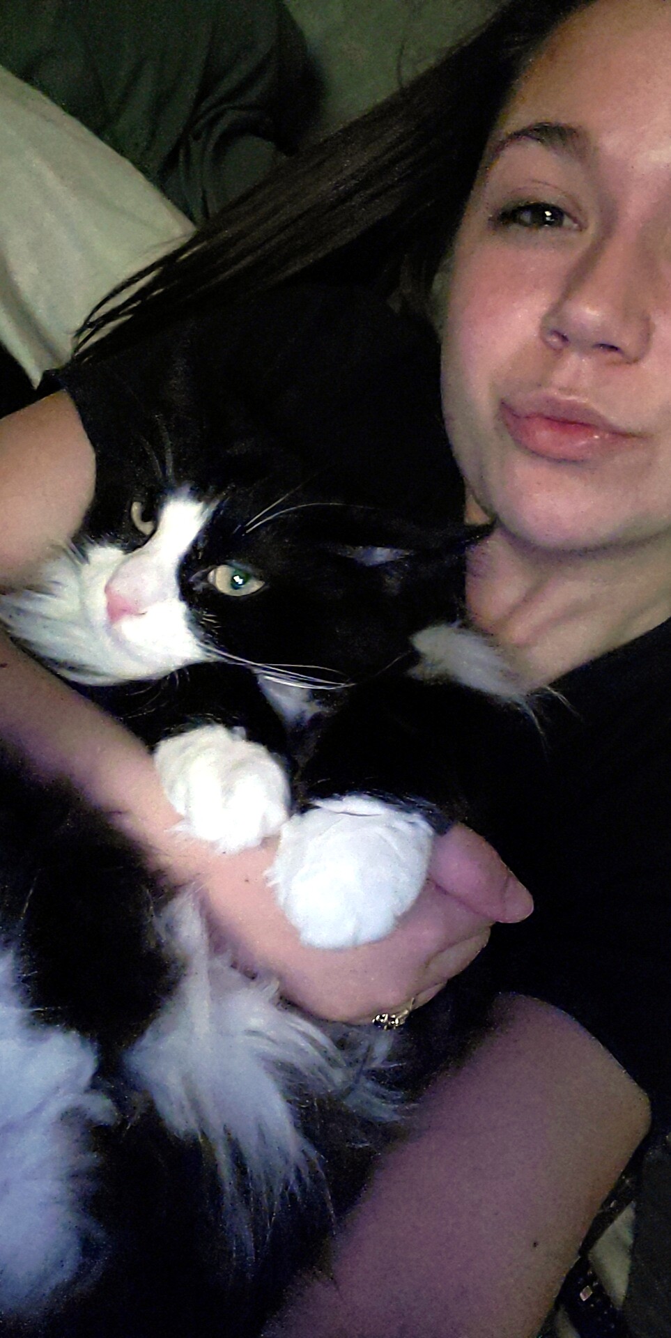 Woman cuddling a black-and-white cat while resting on a couch.