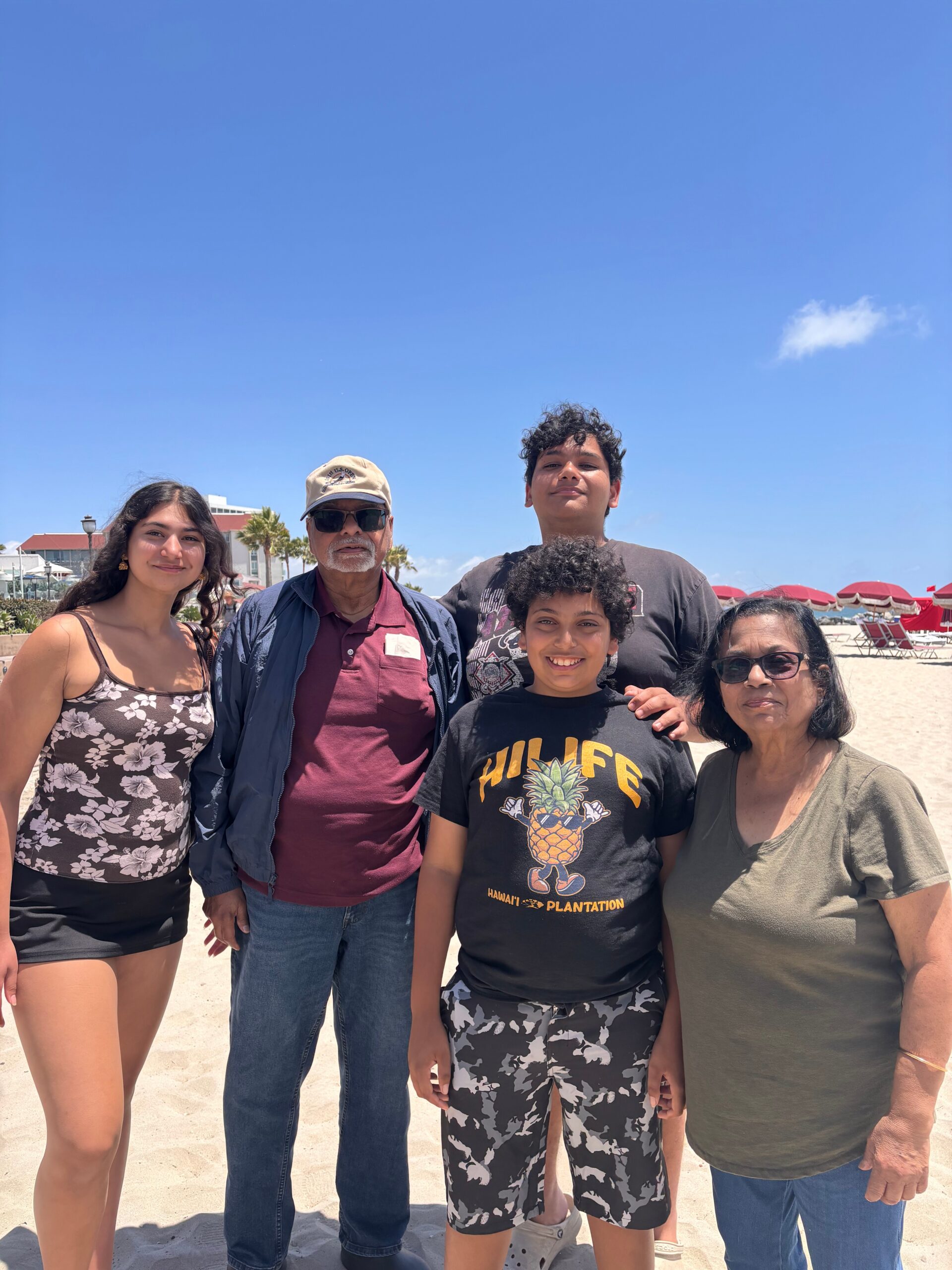 Group of five people posing on a sunny beach under a clear blue sky, smiling at the camera.