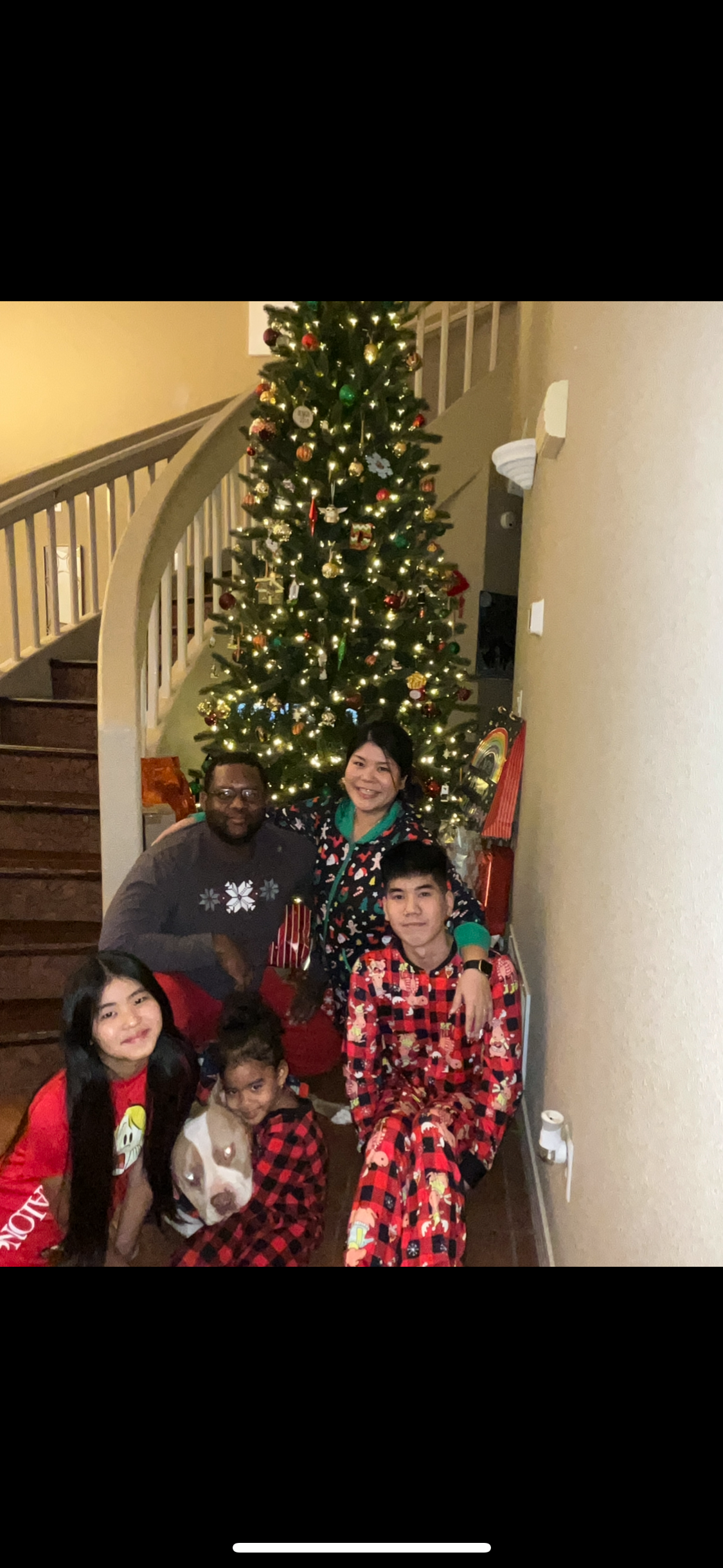 Family of five in matching red plaid pajamas posing in a living room next to a lit Christmas tree.