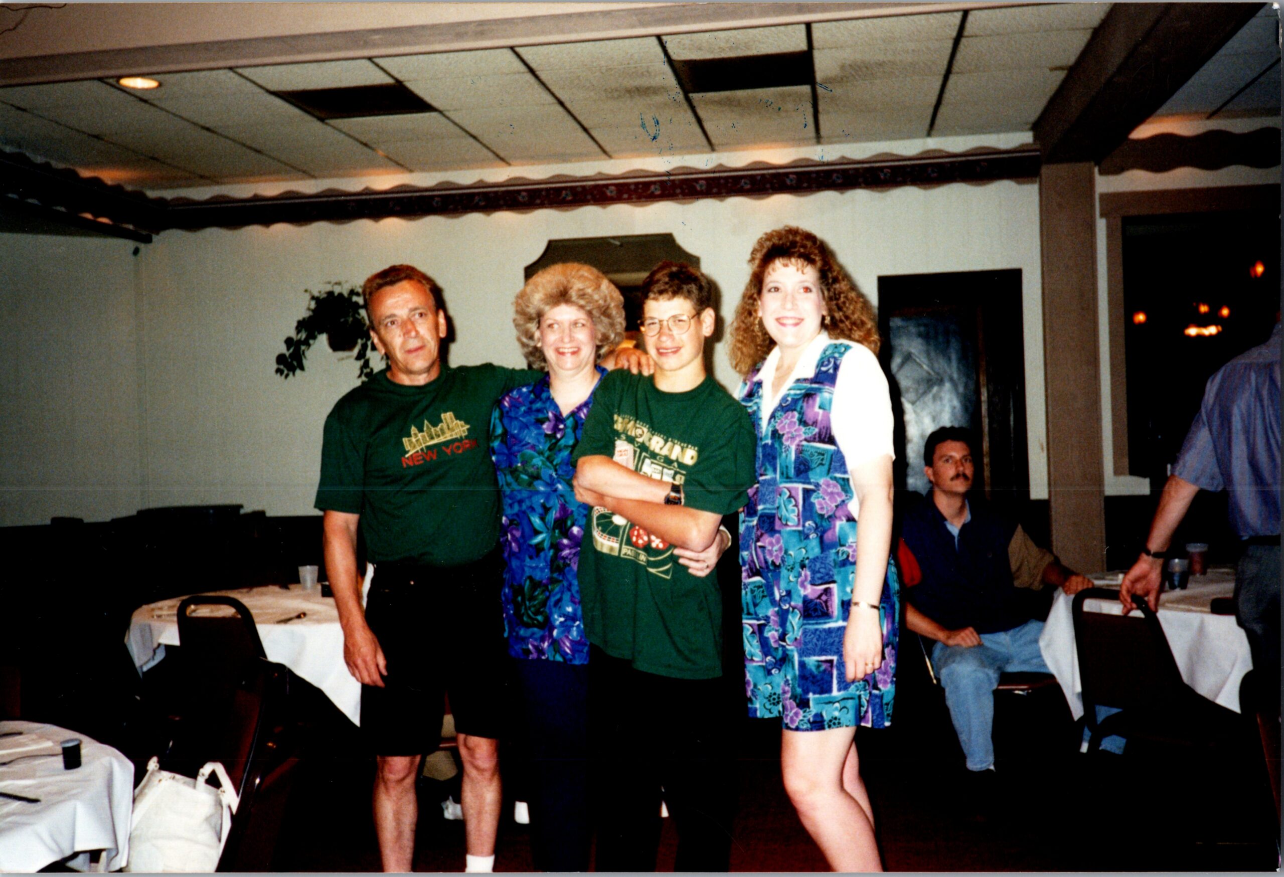 Four adults pose together at a casual social event in a banquet room with tables nearby.
