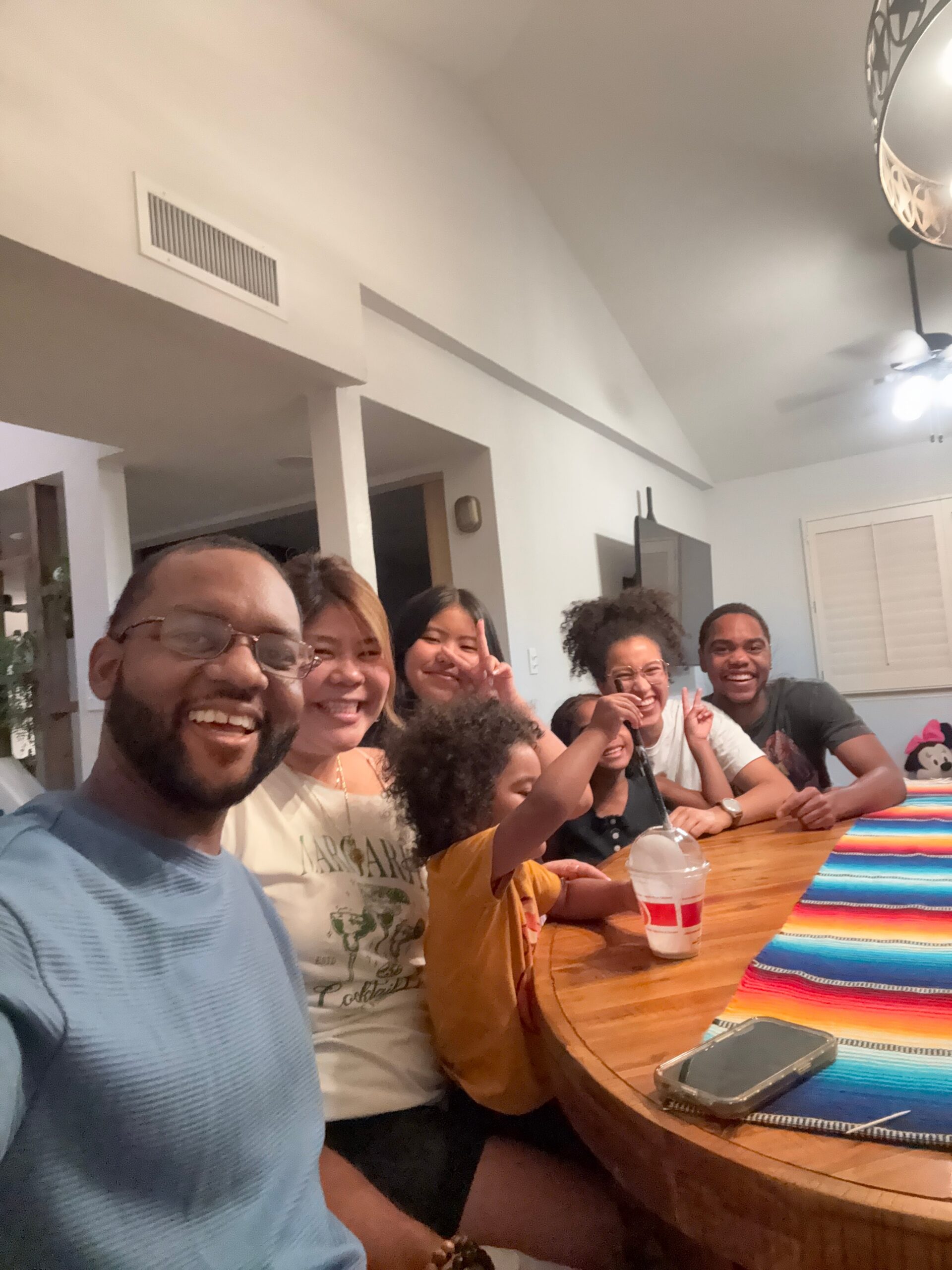 Group of people gathered around a wooden table indoors, smiling at the camera.