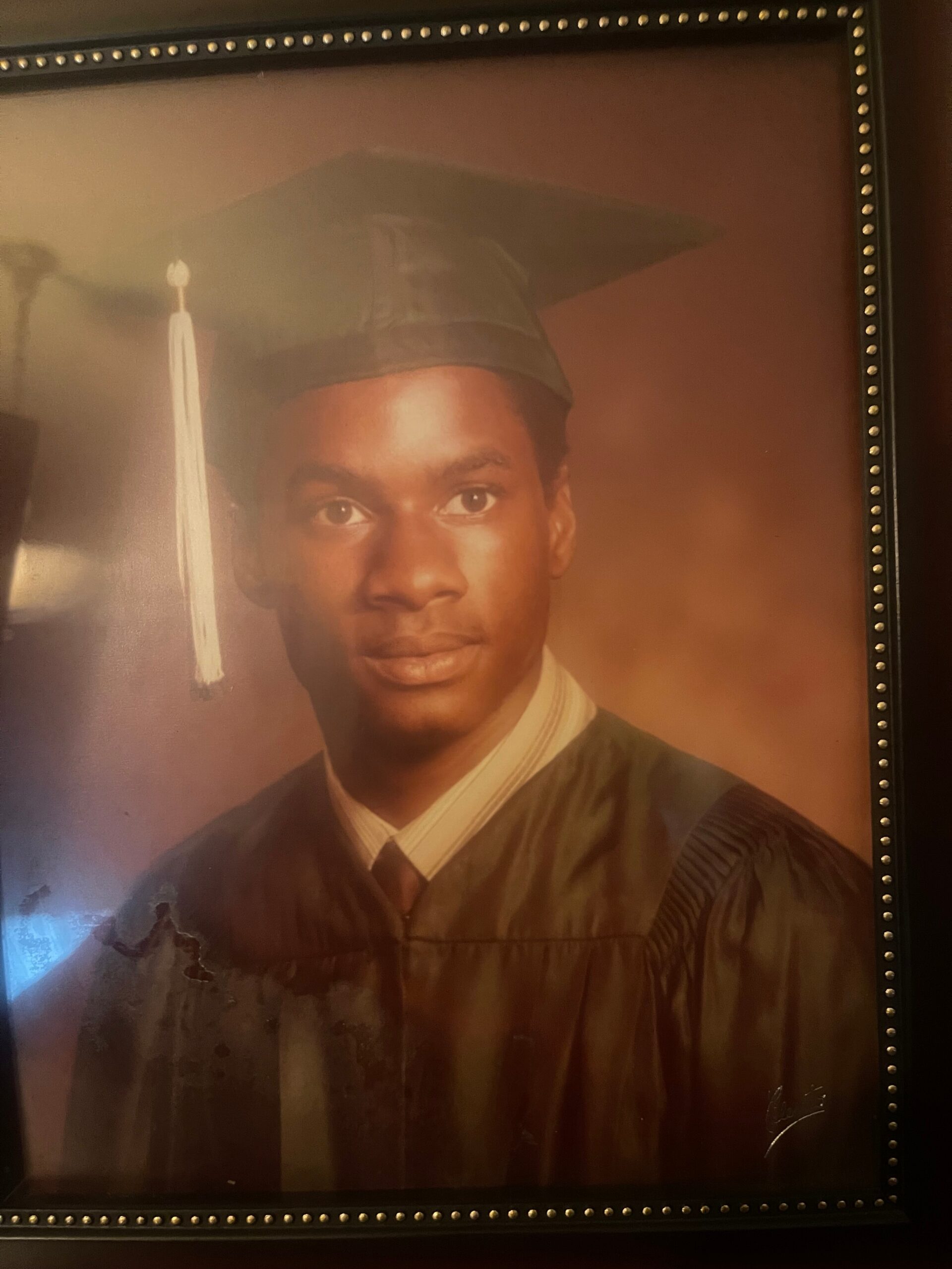 Framed graduation portrait of a young Black man wearing a cap and gown.