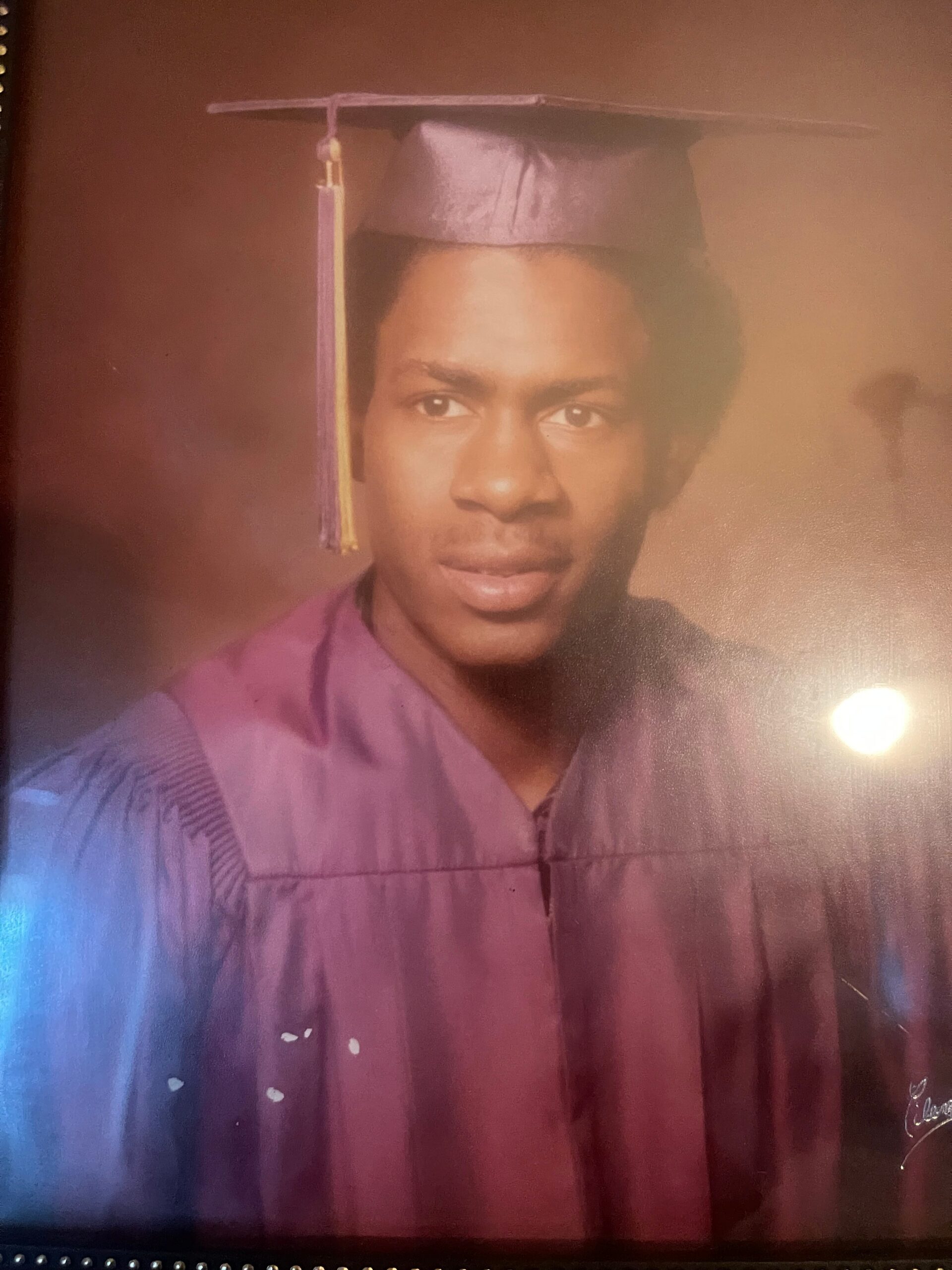 Portrait of a graduate wearing a purple cap and gown, tassel hanging to the left, facing the camera in a studio setting.