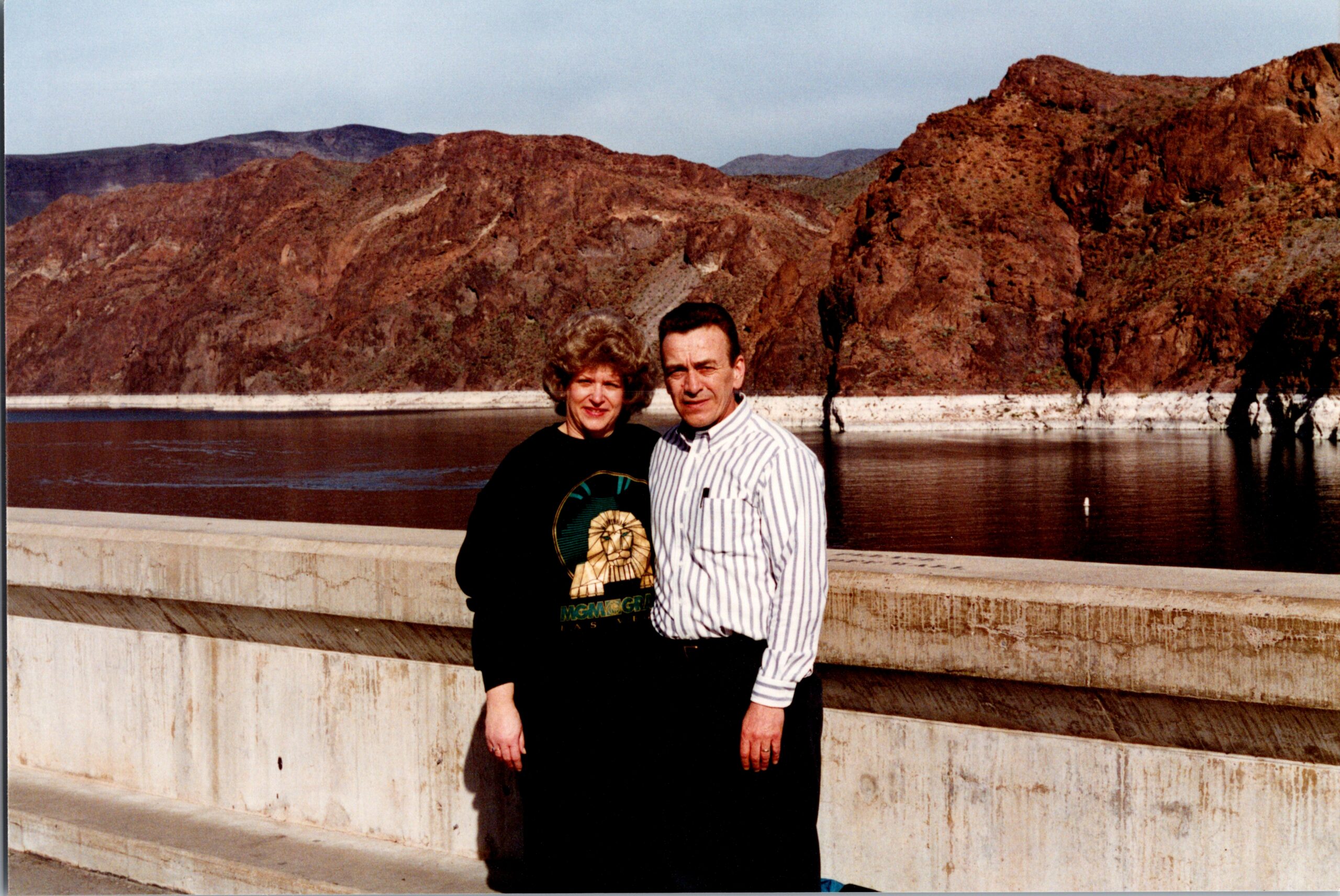 Couple posing together on a concrete railing with red rocky cliffs in the background.