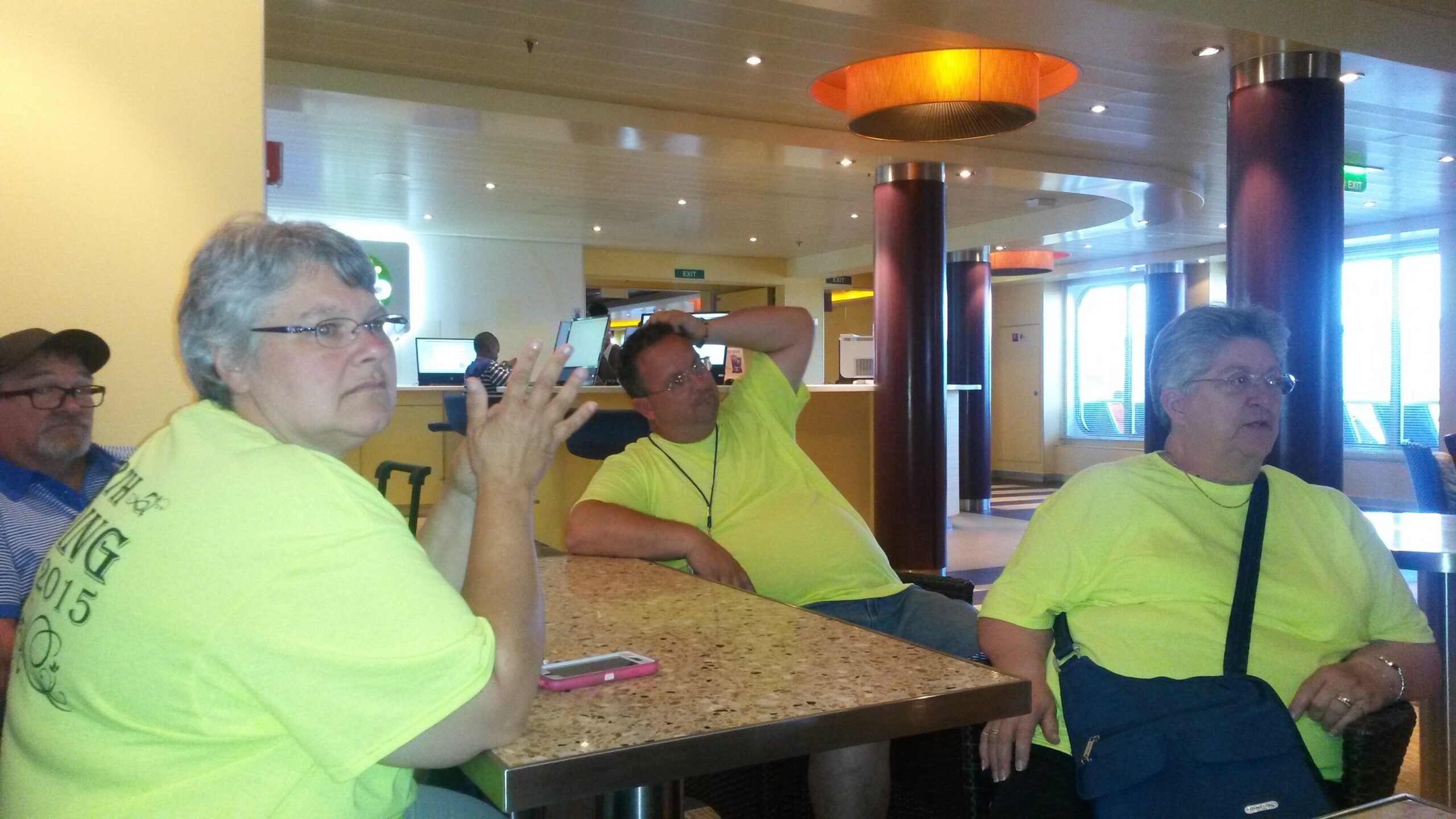 Three seniors in bright yellow shirts sit at a speckled counter in a sunny, modern lounge with purple columns.