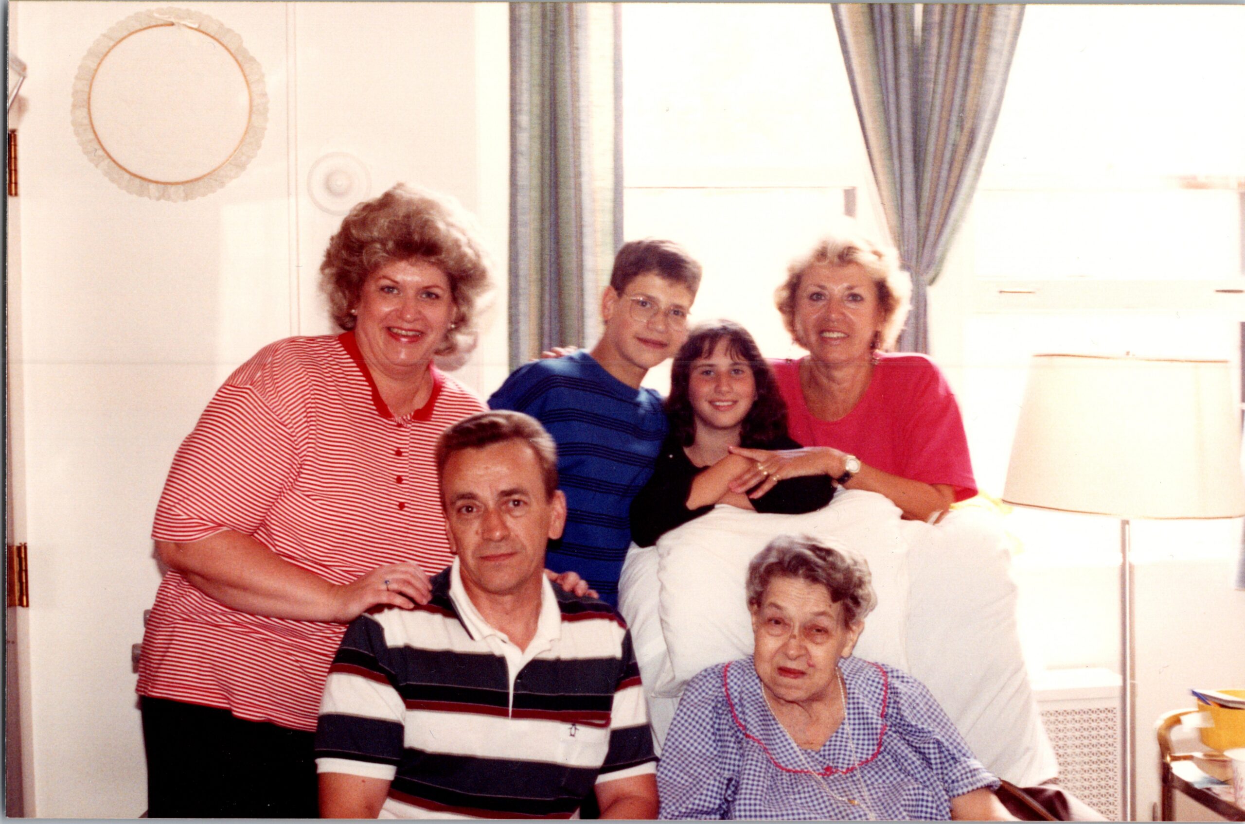 Group portrait of six family members posing together in a living room window-lit setting.