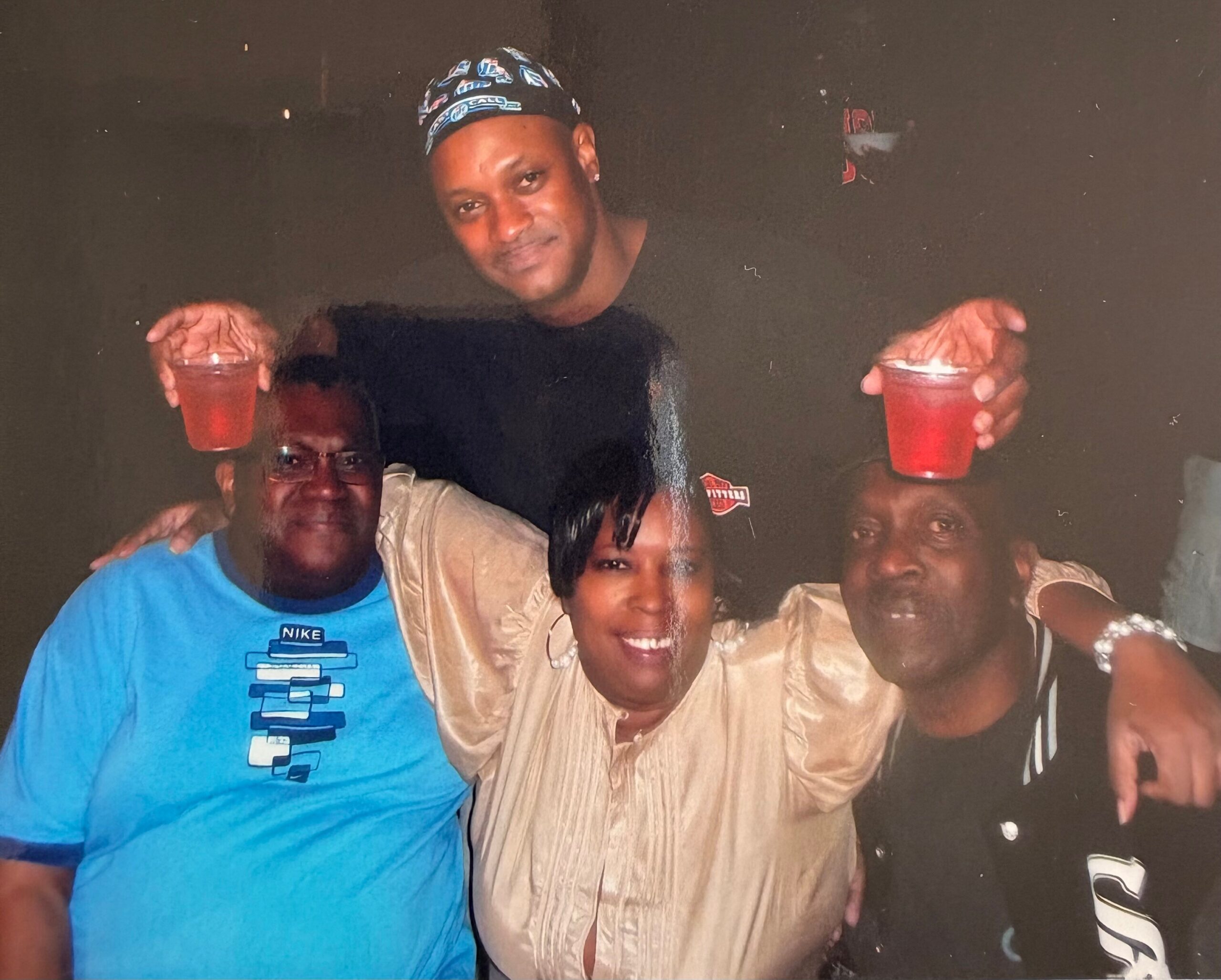 A group of friends posing for a casual photo, holding red drinks in plastic cups and smiling at the camera.