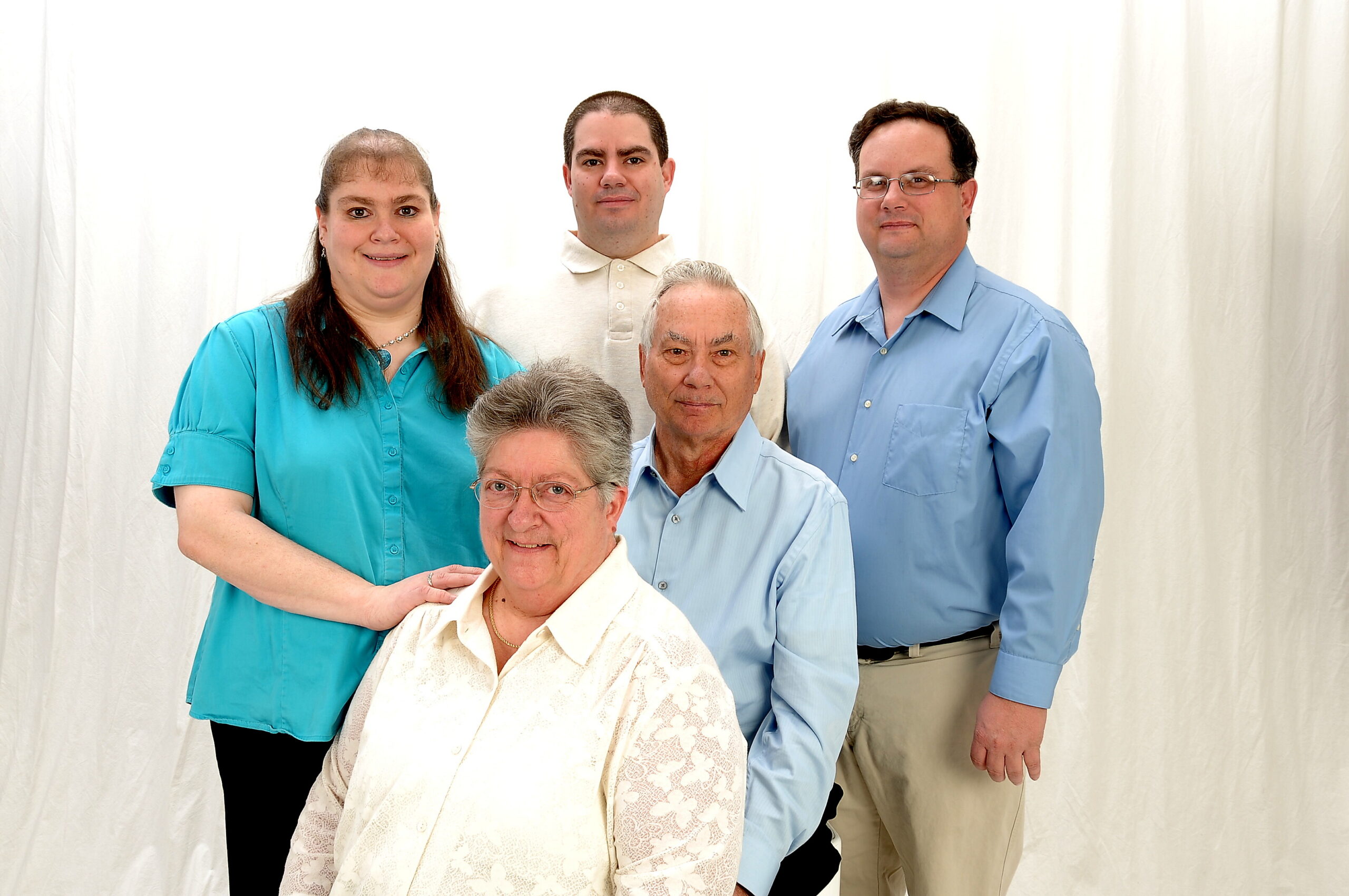 Group of five adults posing for a portrait against a white backdrop, smiling, wearing casual business attire (blue shirts and light polo).