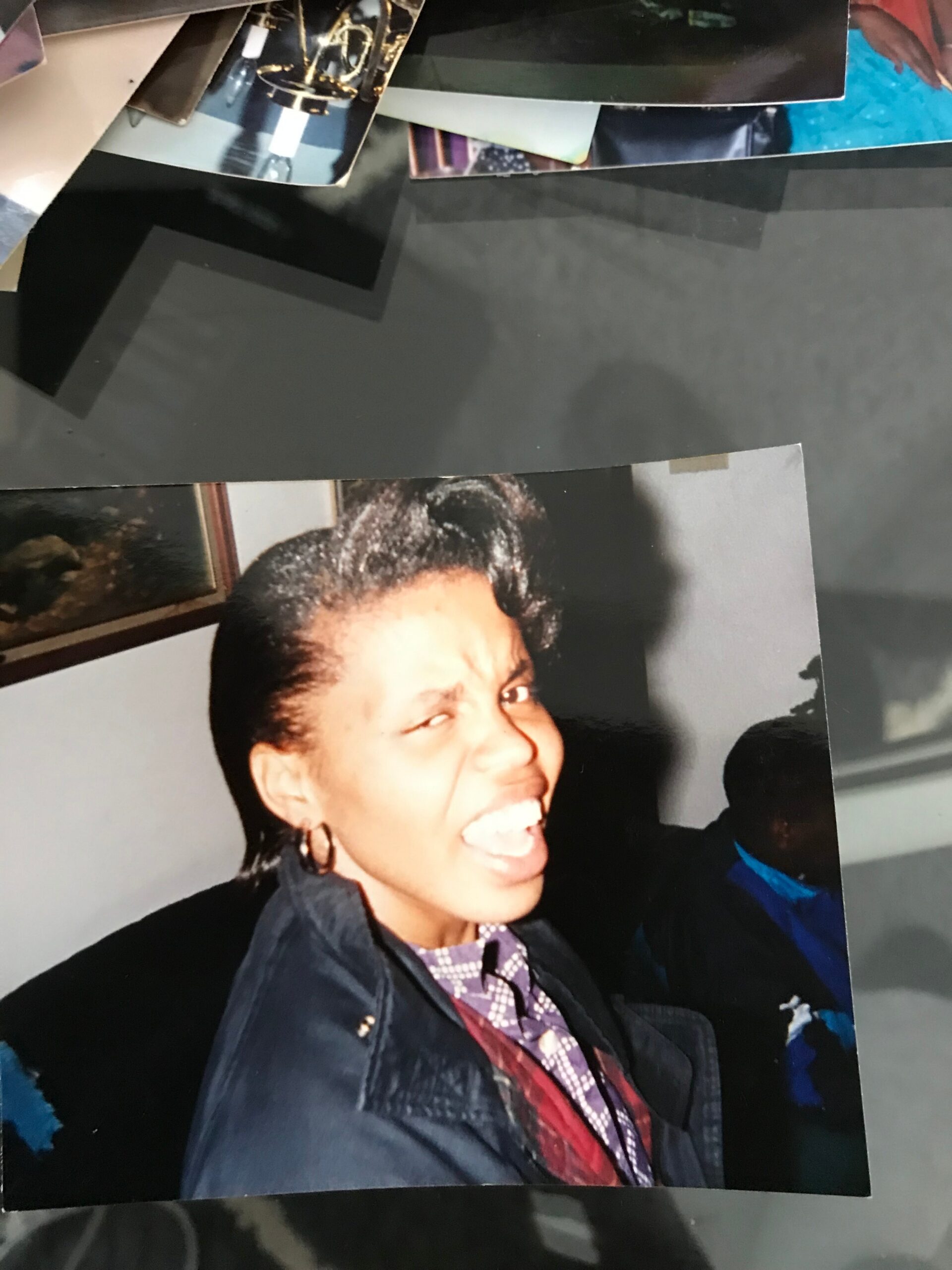 Smiling woman in a dark blazer and purple plaid shirt, photographed indoors among stacked photos in a collage.
