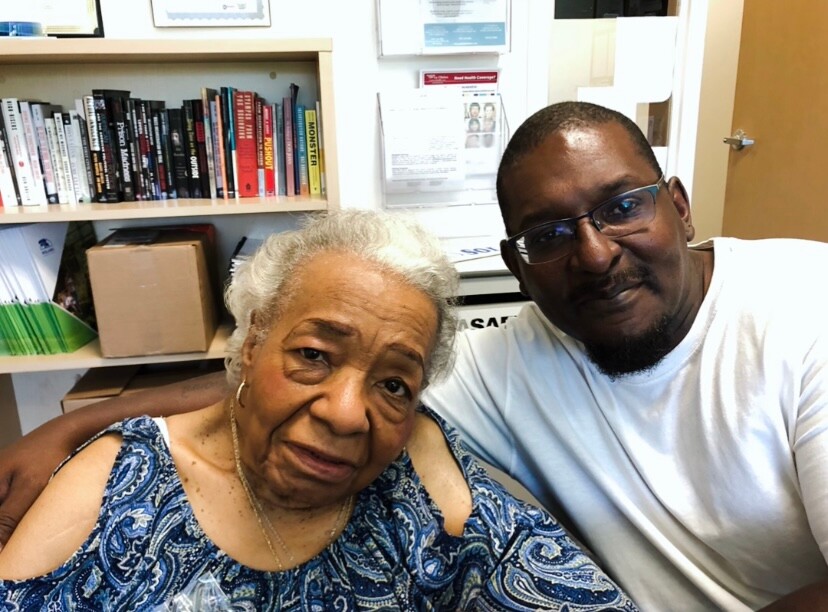 Two people smile for a selfie in a room with bookshelves in the background.