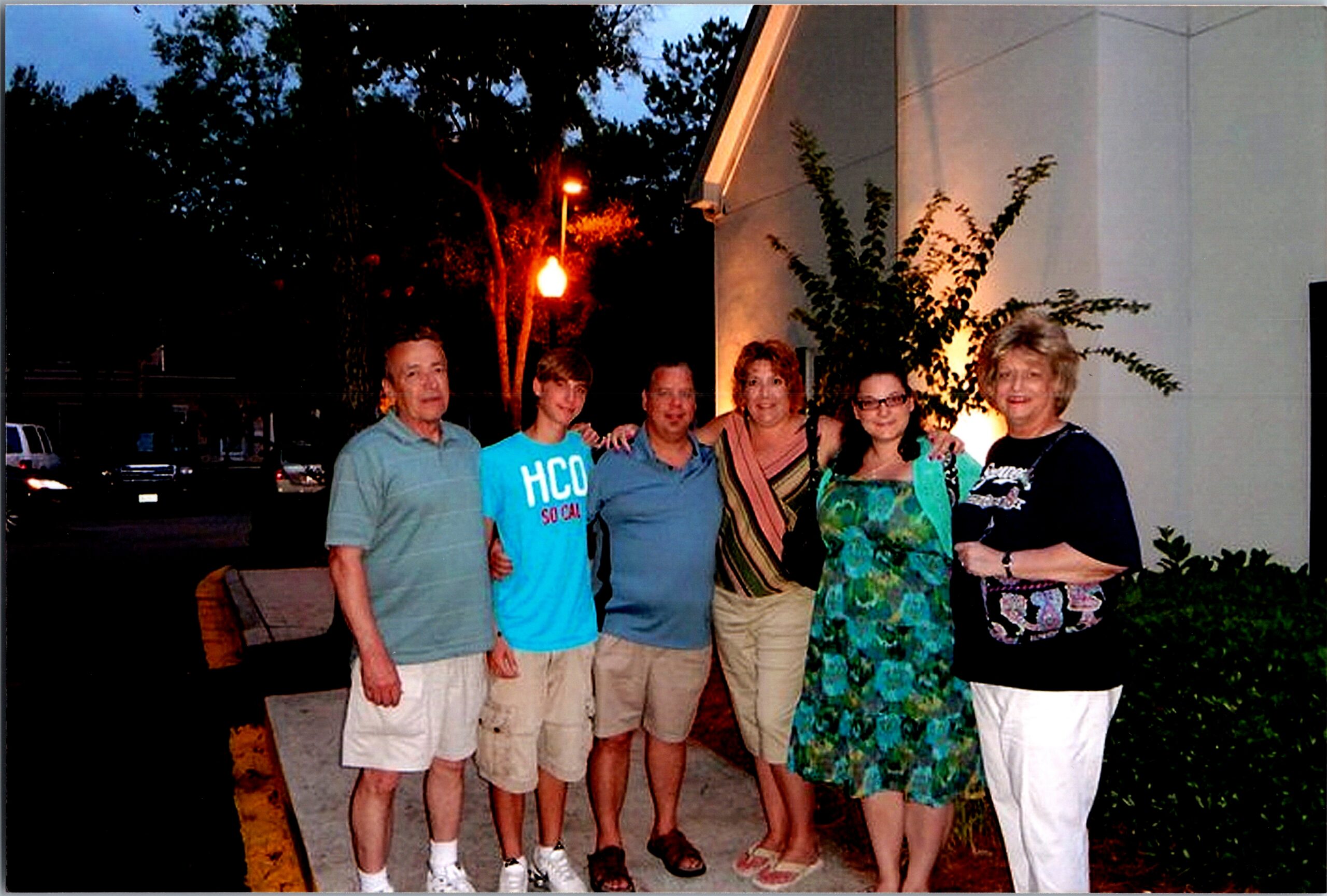 Six people posing together outside a building at dusk, smiling for the photo (group portrait).