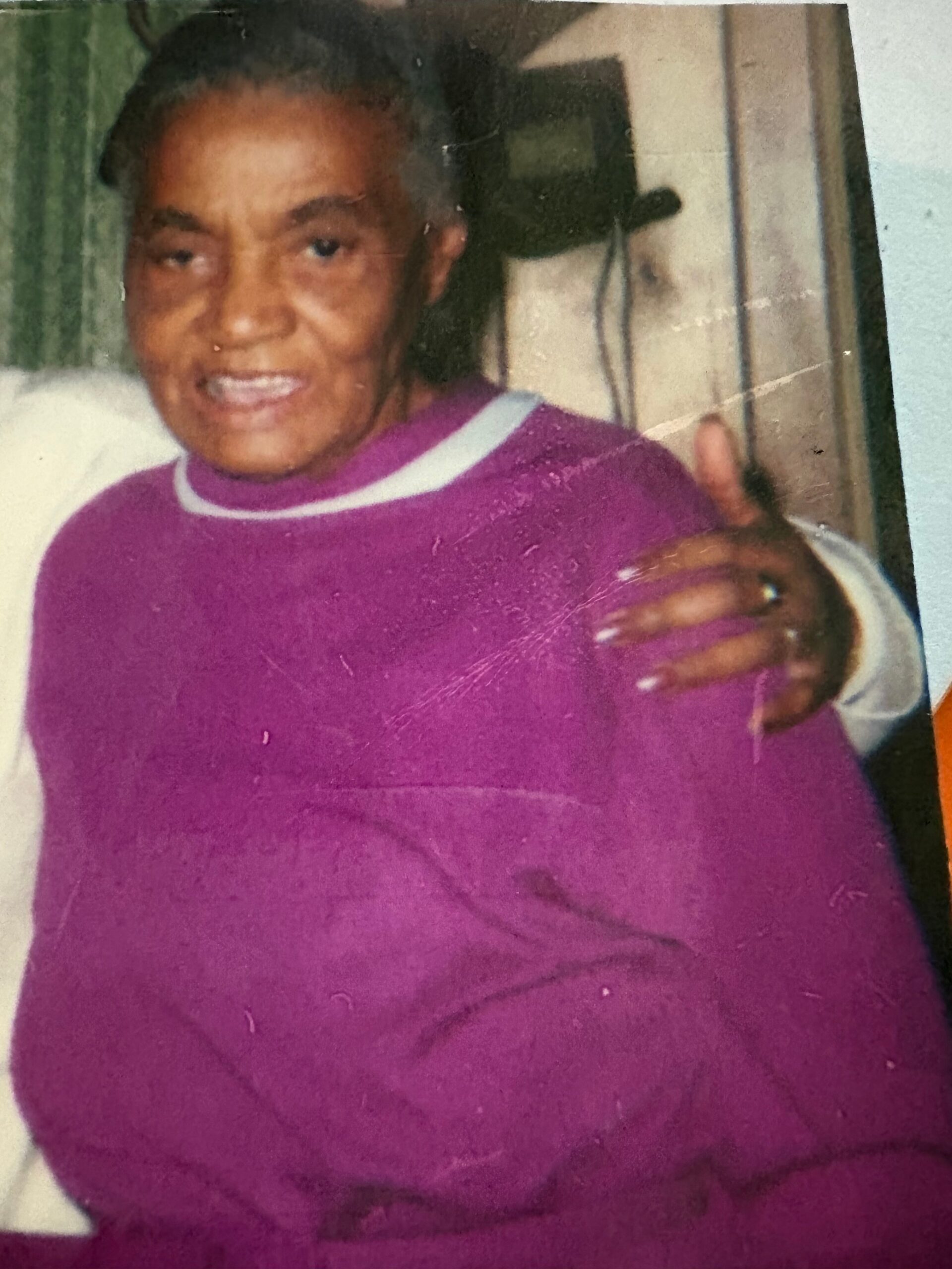 Smiling person in a purple sweater giving a thumbs up gesture toward the camera.
