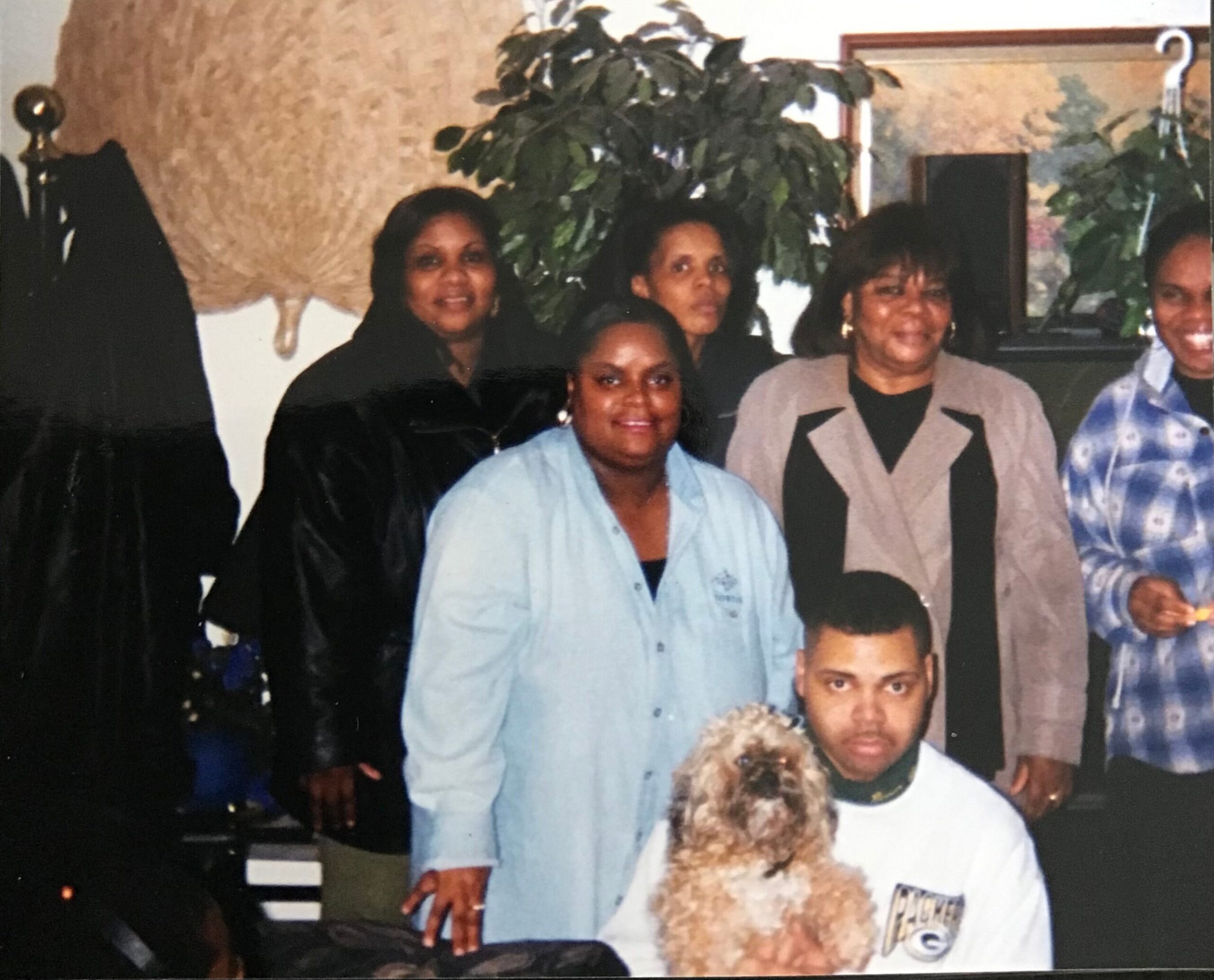 Group of people posing for a photo at an indoor gathering, with a large plant behind them.